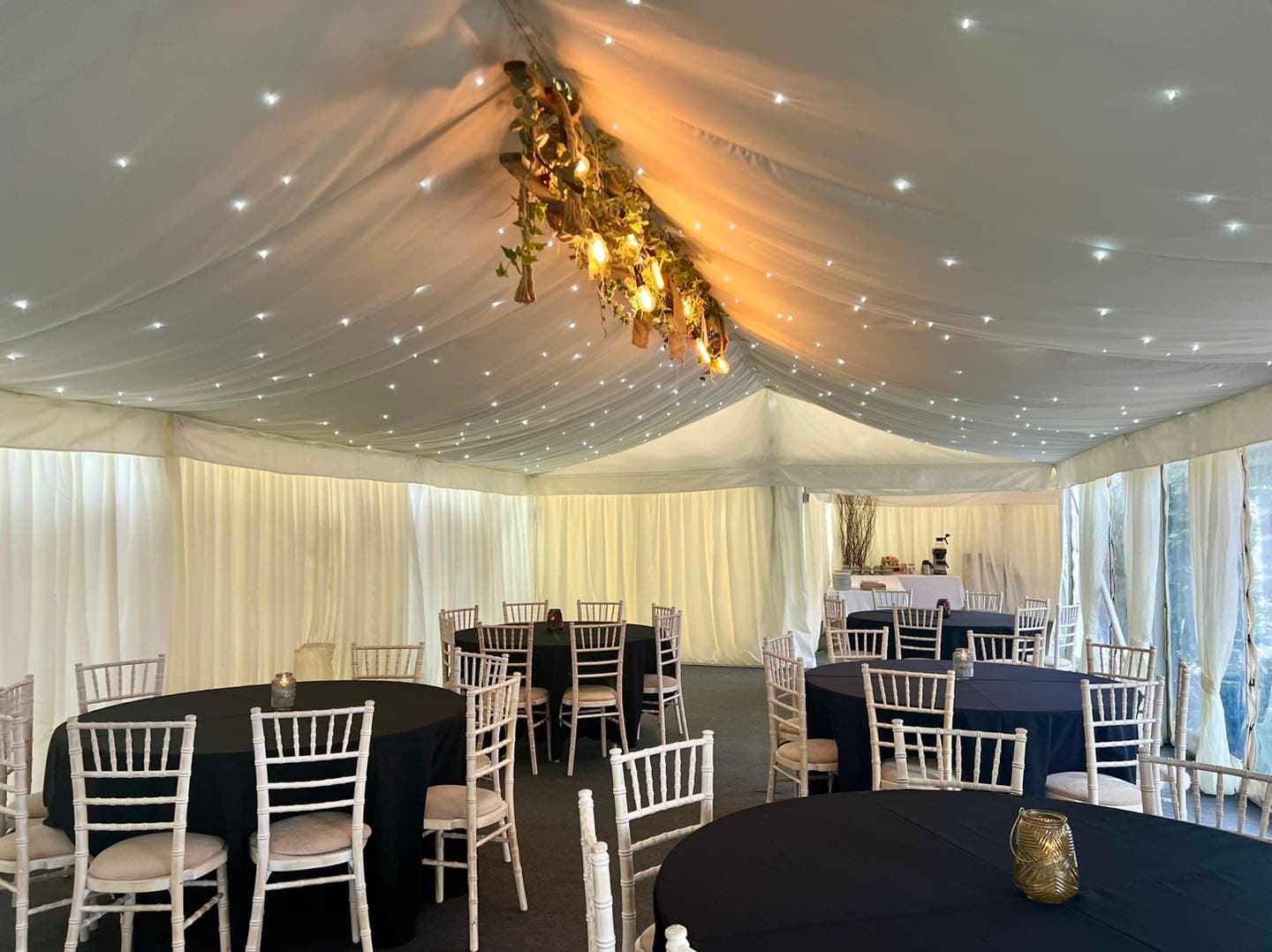 White marquee interior with round black-clothed tables, chiavari chairs and starlit ceiling