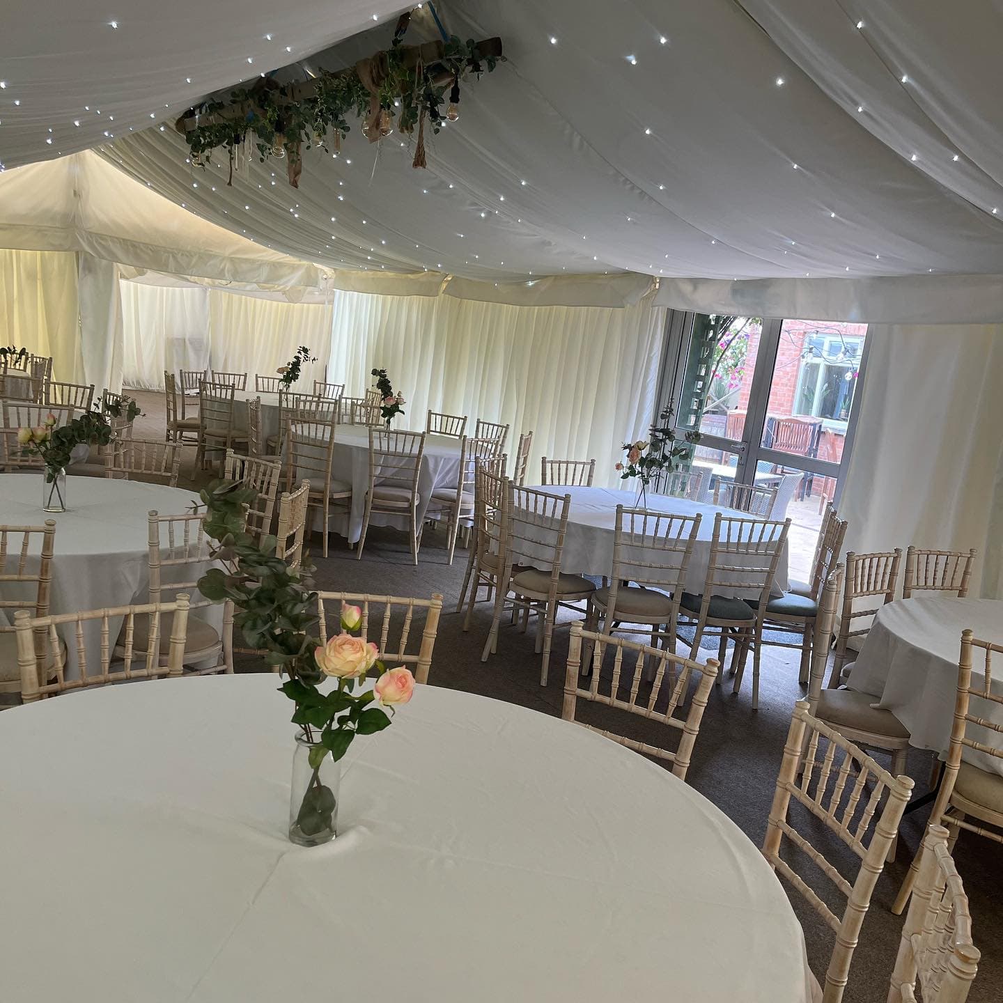 Marquee interior with round tables, chiavari chairs and fairy lights in the ceiling