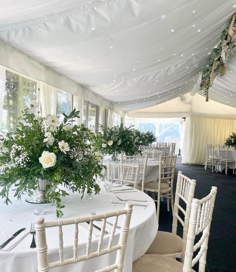 Marquee interior with round tables, chiavari chairs and tall white floral centrepieces