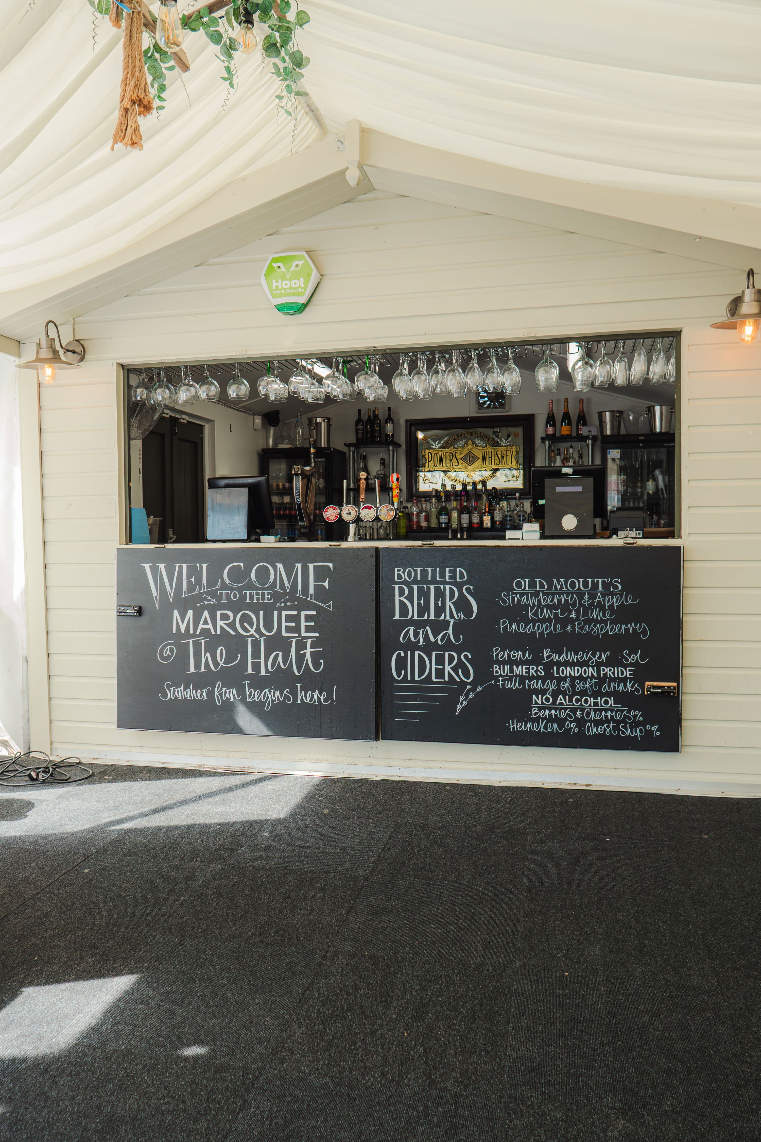 The Brampton Halt marquee bar with chalkboard menus and wine glasses overhead.
