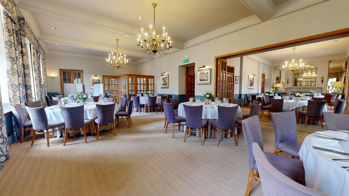 Elegant private dining room with round tables, brass chandeliers and blue upholstered chairs.