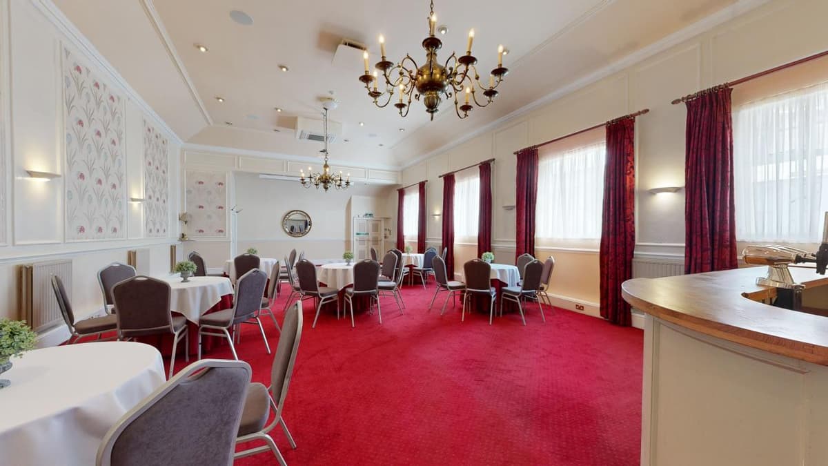Function room with round tables, red carpet and brass chandeliers at The Castle Hotel Taunton.