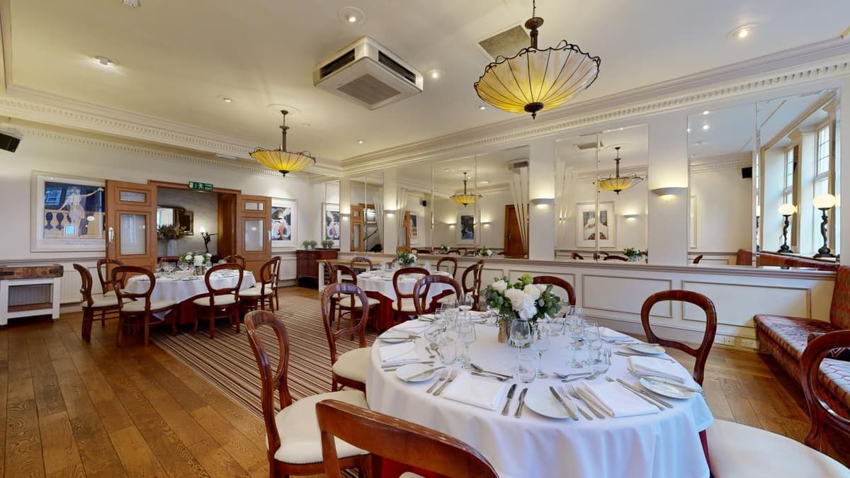 Formal dining room with round tables, white linen and Tiffany-style pendant lights.