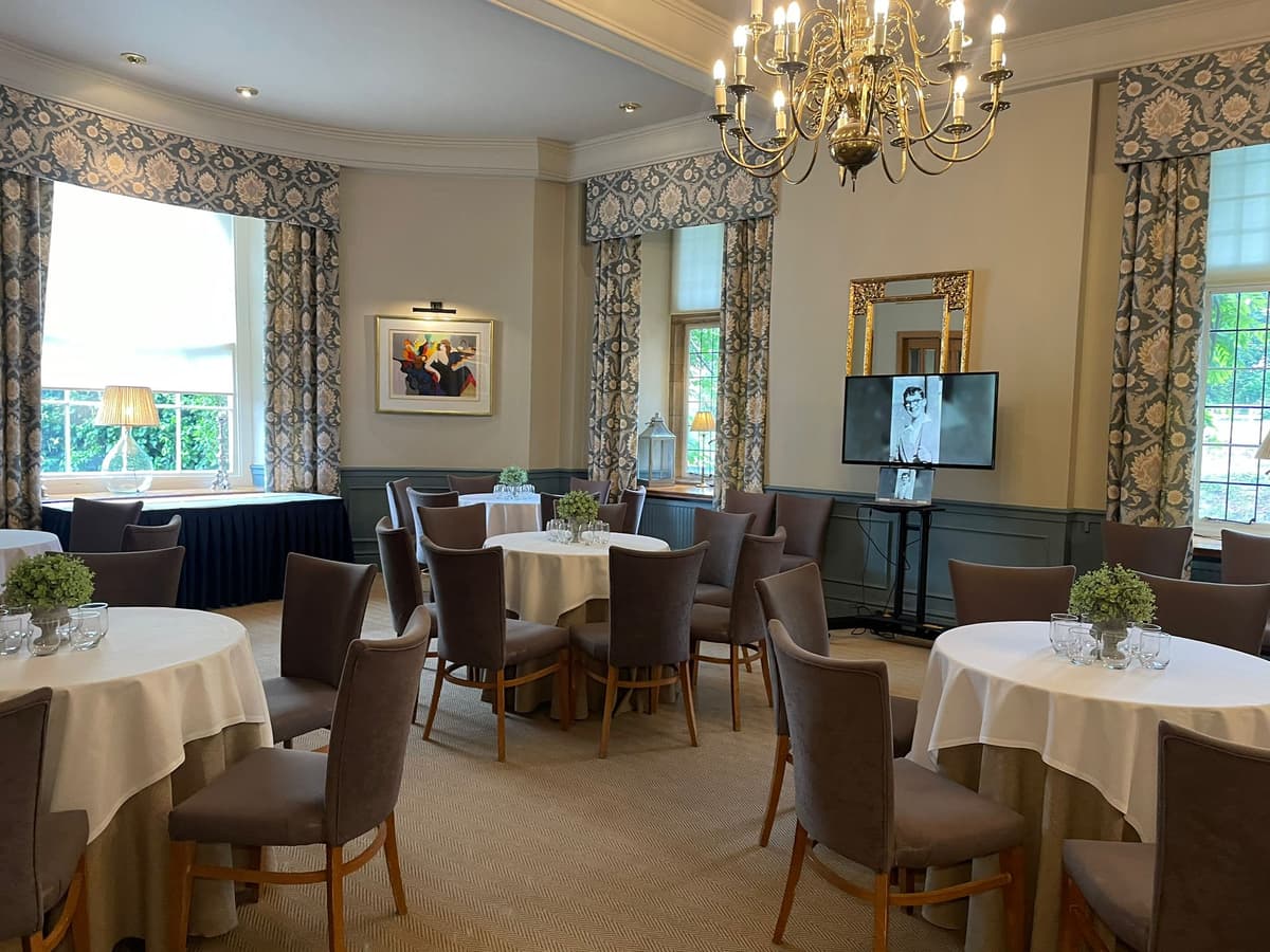 Private dining room with round tables, grey chairs and a brass chandelier.