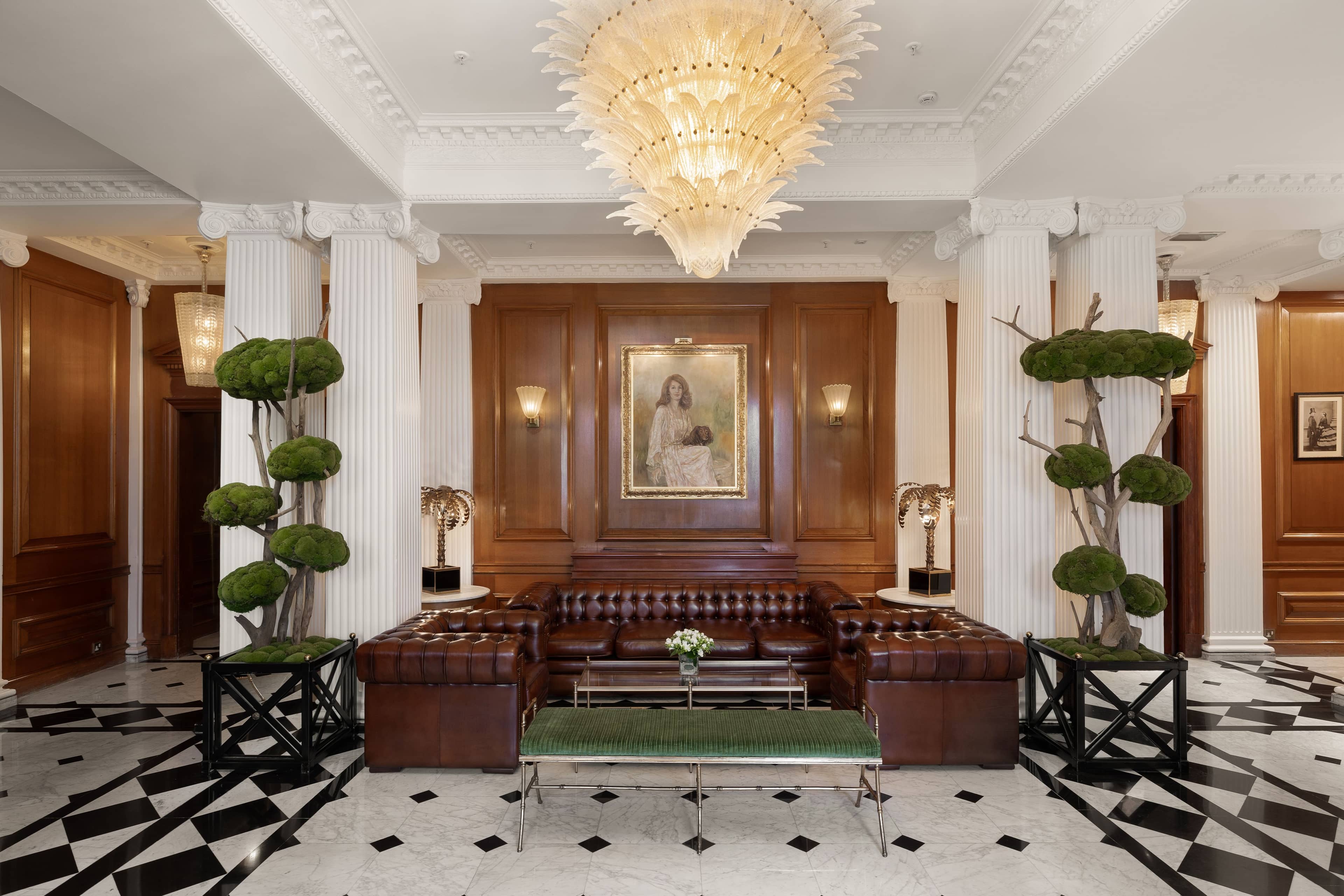 Hotel lobby with leather Chesterfield sofas, marble floor, columns and a large chandelier.