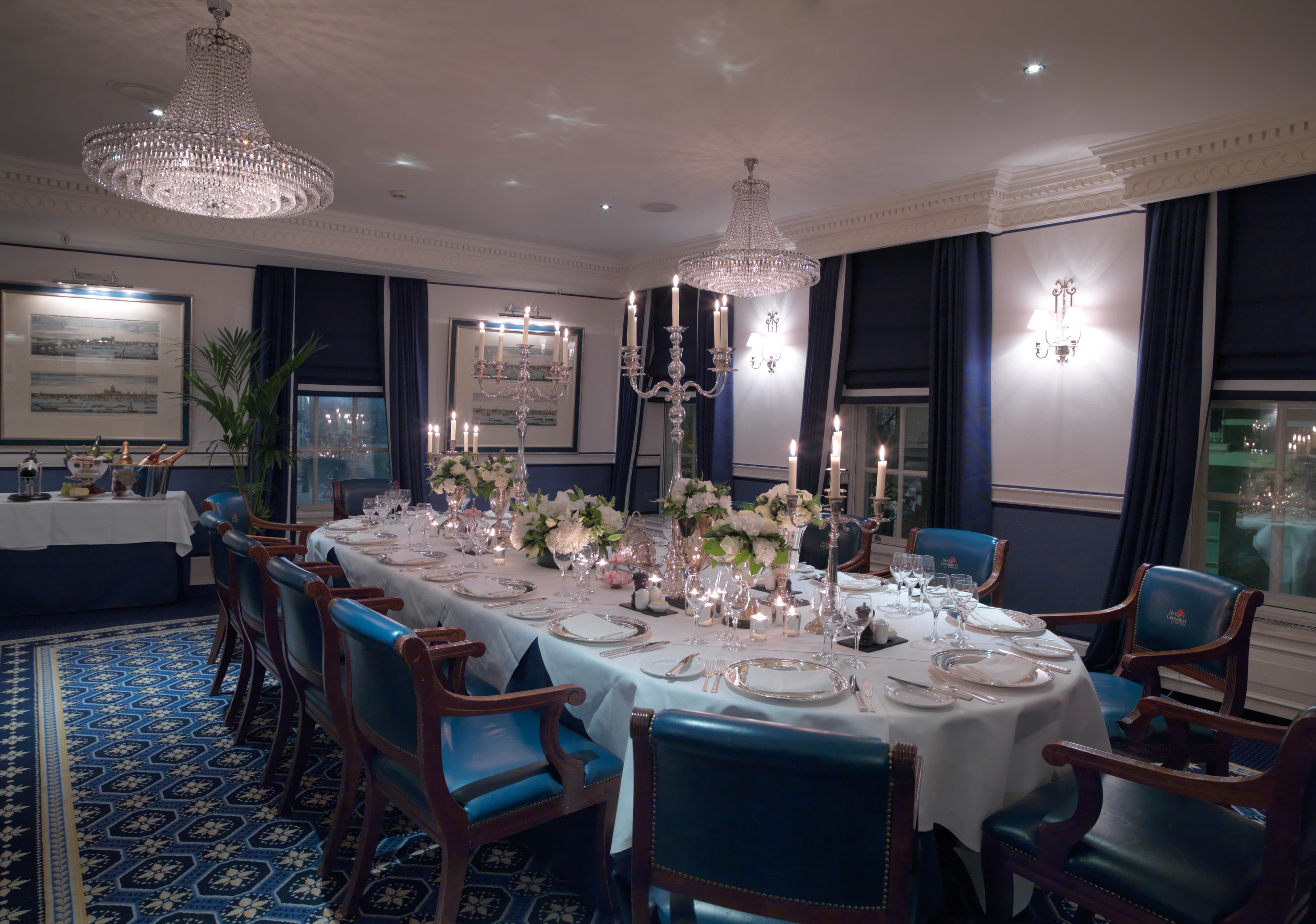 Private dining room with long candlelit table, crystal chandeliers and blue leather chairs.