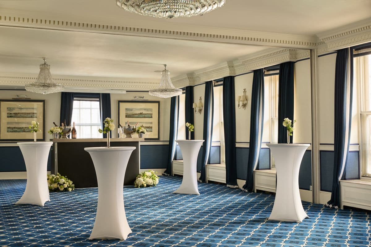 Elegant function room with crystal chandeliers, cocktail tables and blue patterned carpet.