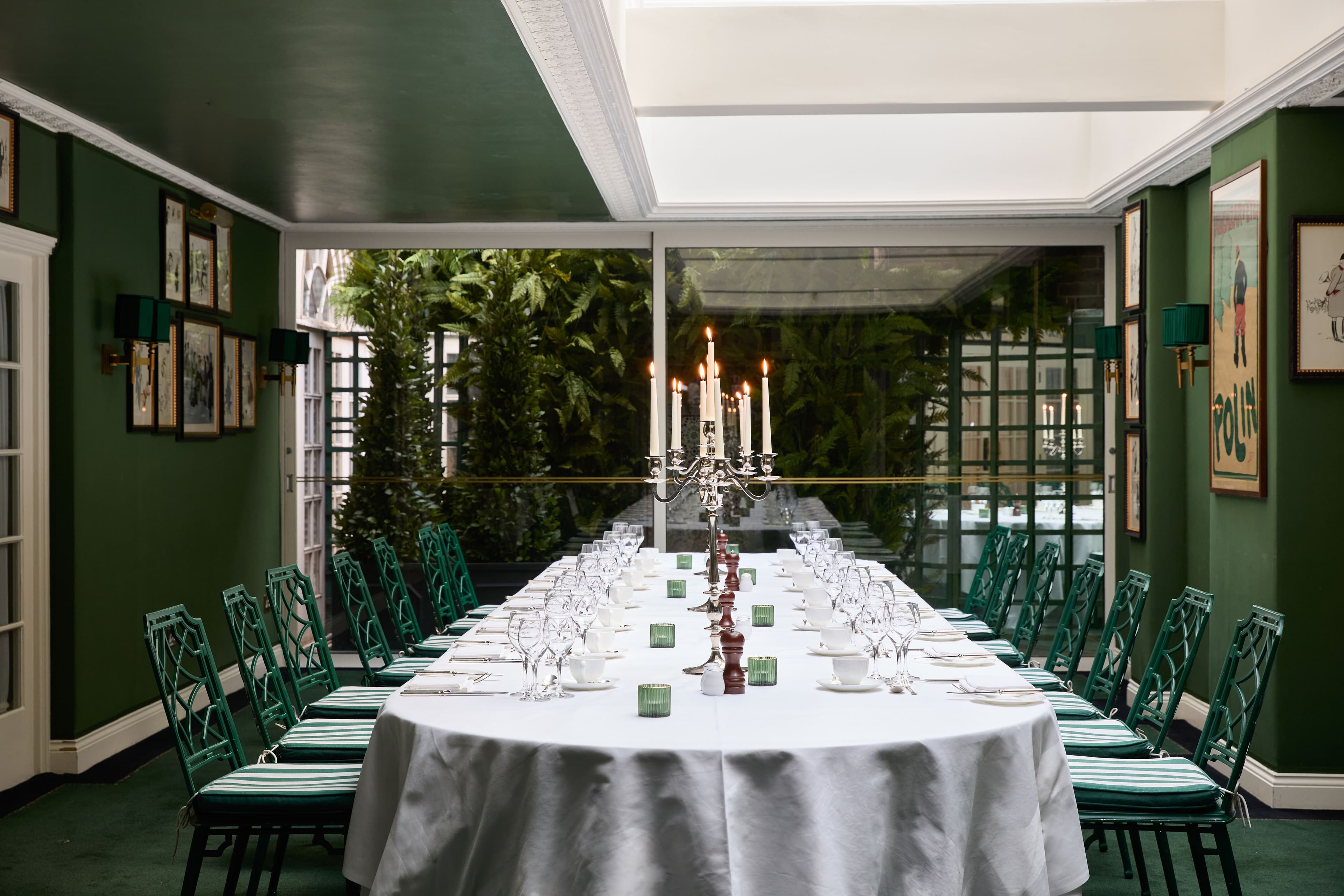 Private dining room with long white-clothed table, candelabra and green Chinoiserie chairs.