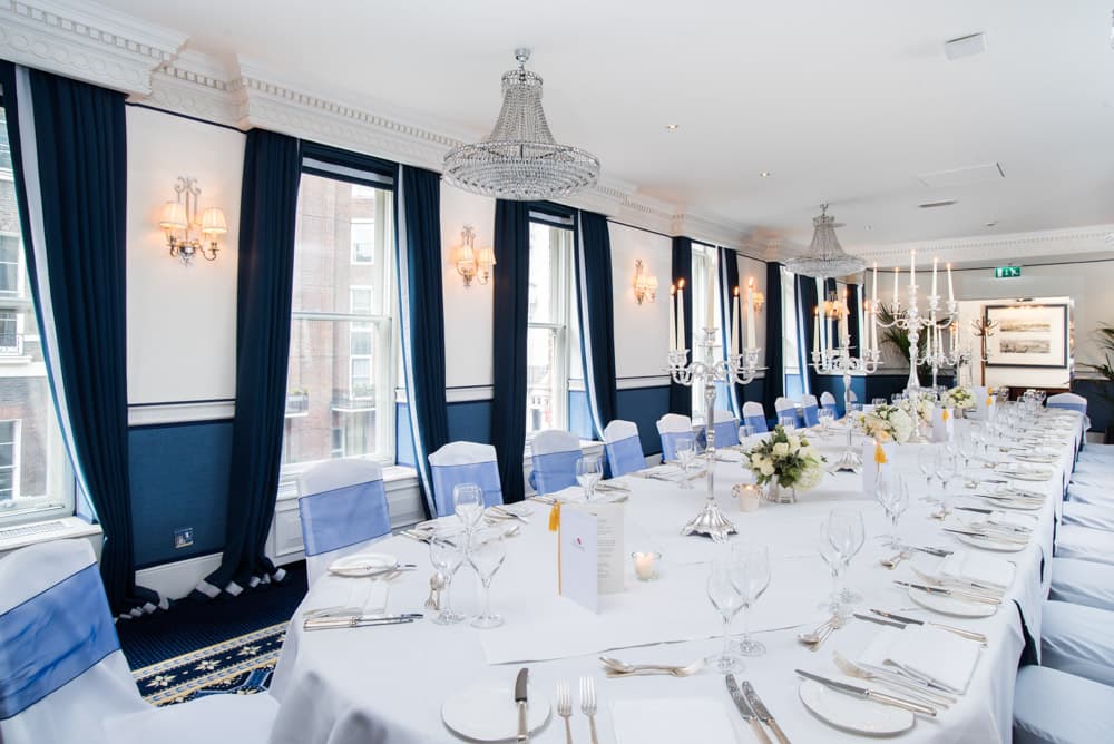 Elegant private dining room with long white-clothed table, crystal chandeliers and blue drapes.