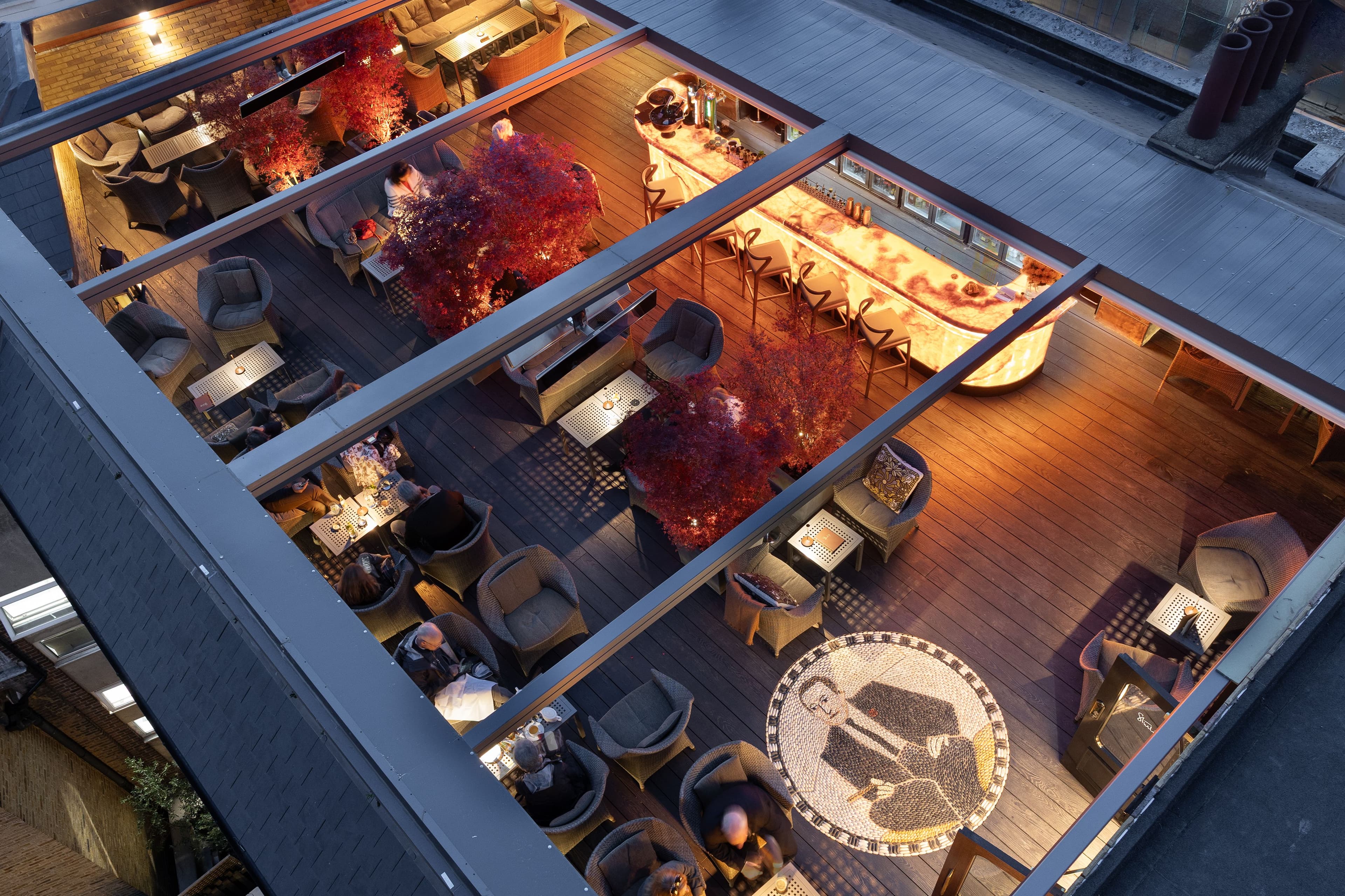 Aerial view of a rooftop terrace bar with red trees and glowing counter