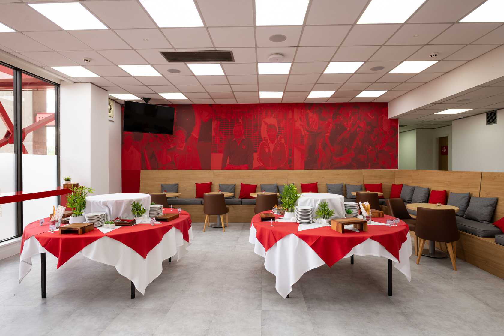 Hospitality suite with red and white dressed tables and a large football mural behind banquette seating.