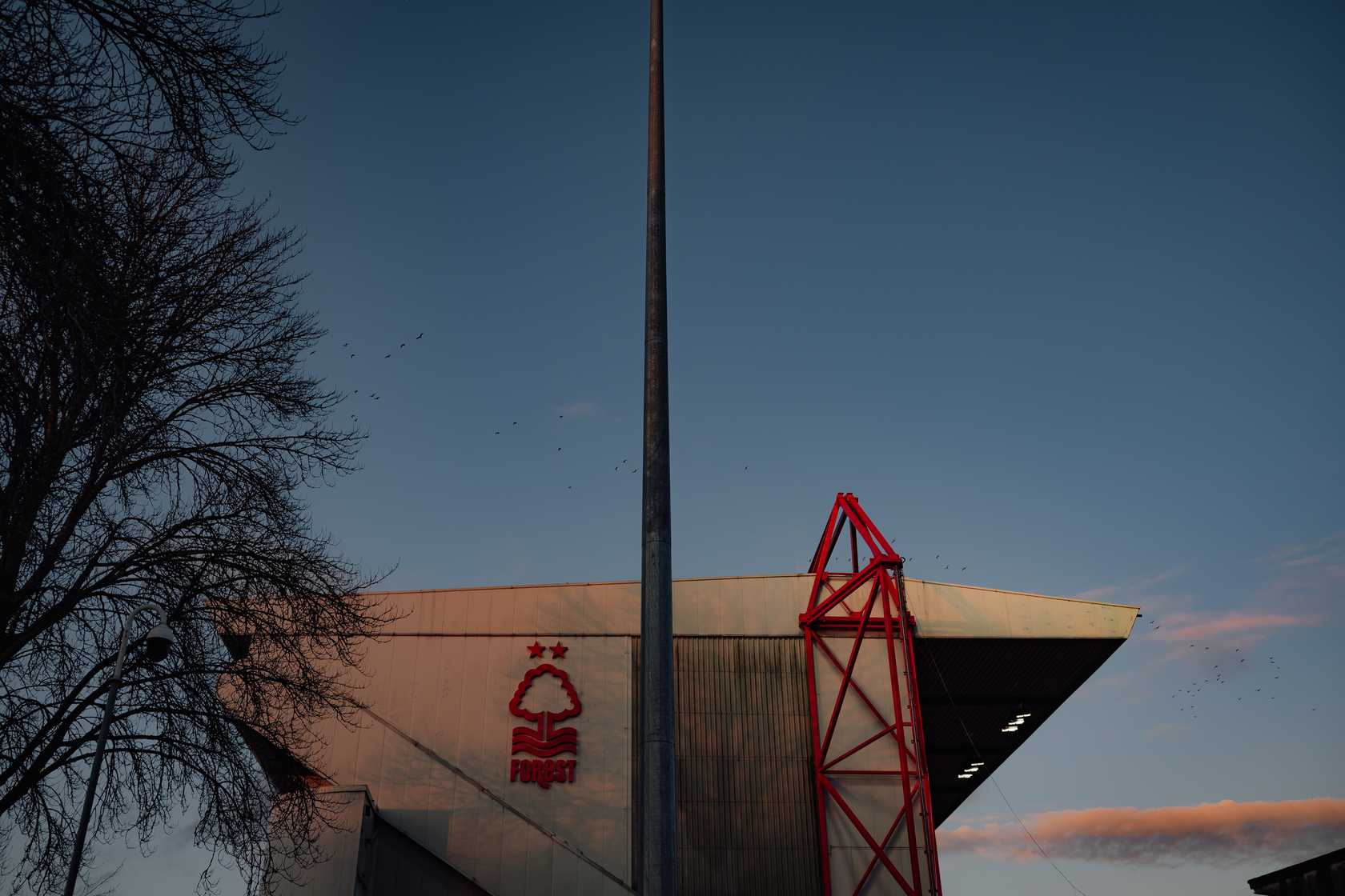 Exterior of The City Ground at dusk showing the Nottingham Forest club crest.