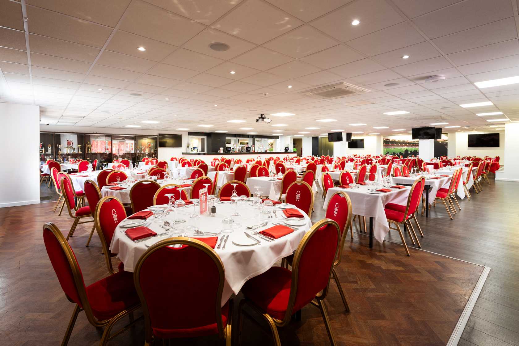 Banqueting suite with round tables, red upholstered chairs and white tablecloths laid for dining.