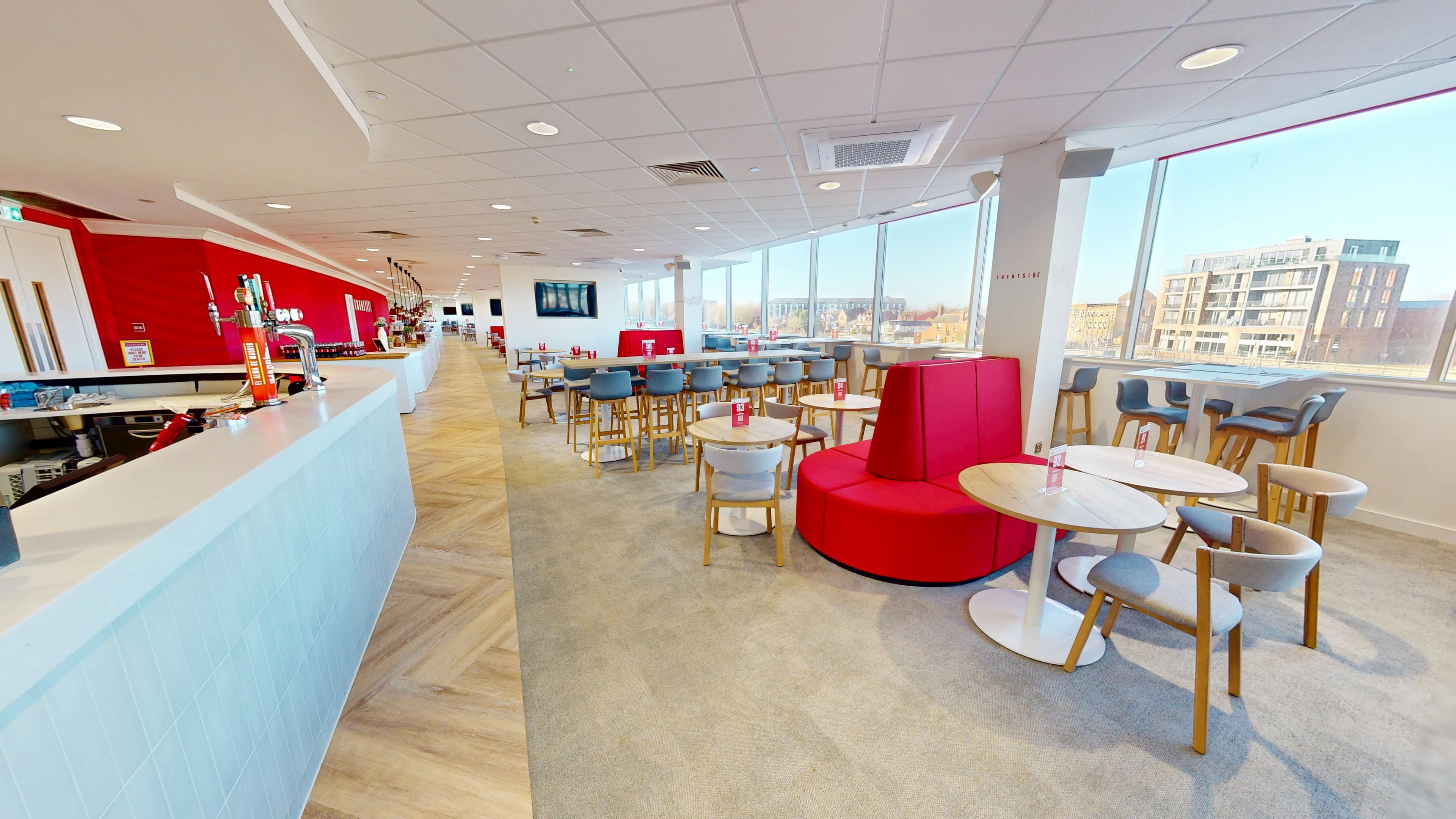 Bright hospitality lounge with bar, round tables, red seating and city views.