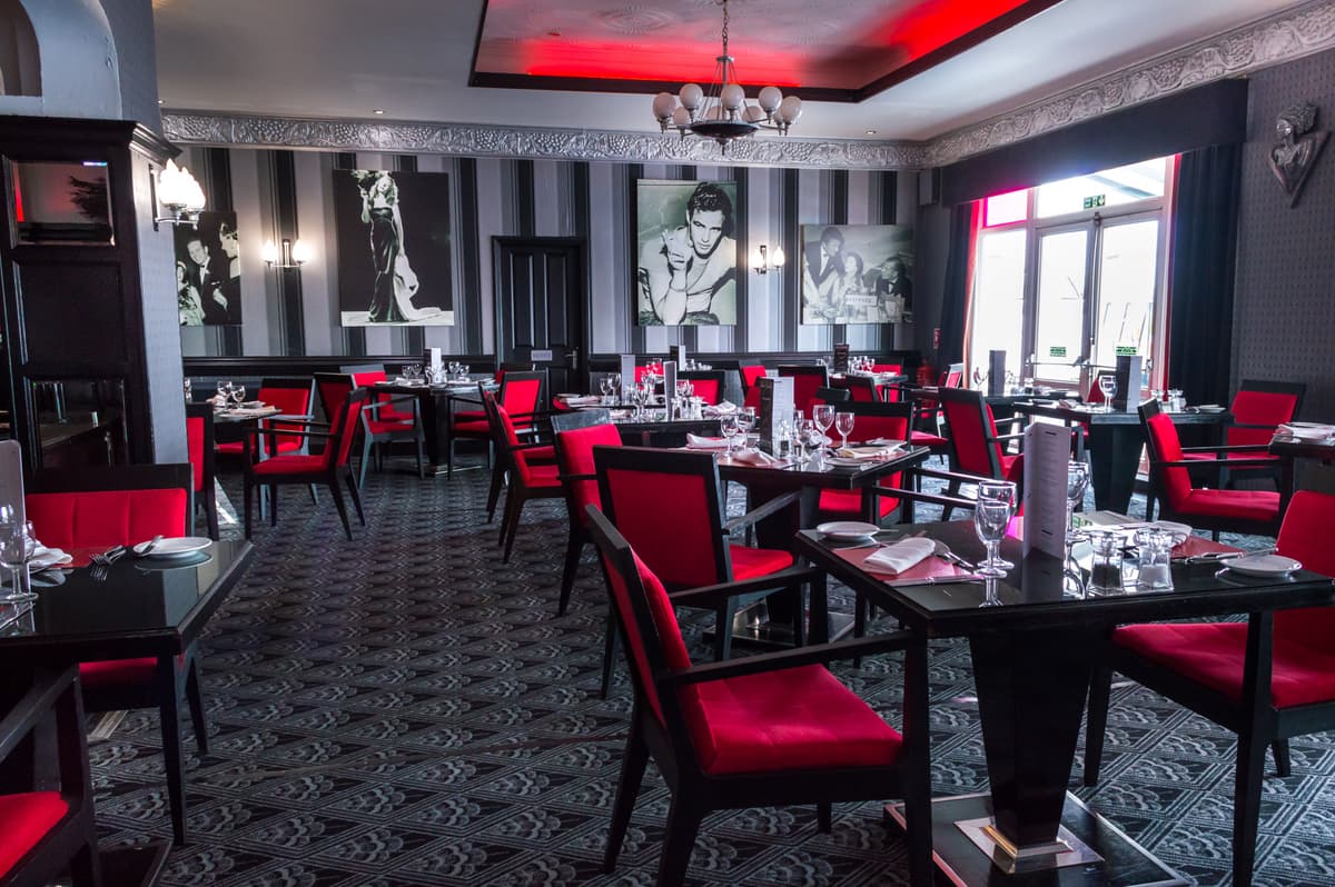 Restaurant dining room with red chairs, dark tables and black-and-white Hollywood prints on walls.