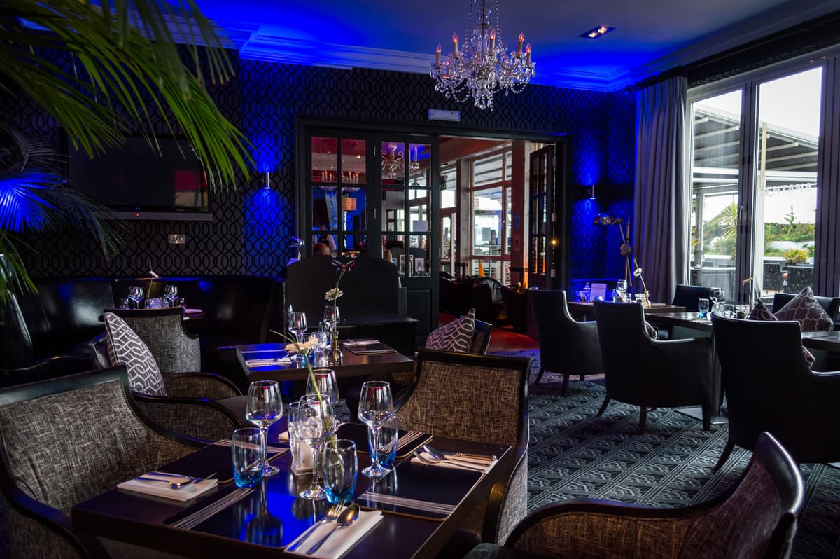 Dimly lit restaurant interior with laid tables, a crystal chandelier and blue uplighting.