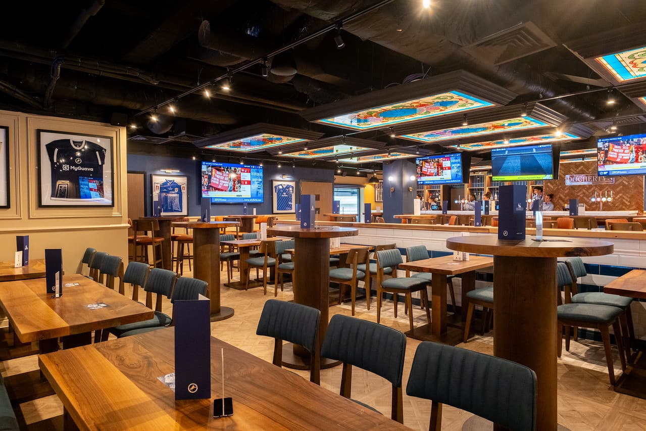 Spacious sports bar interior with wooden tables, blue chairs and multiple TV screens.