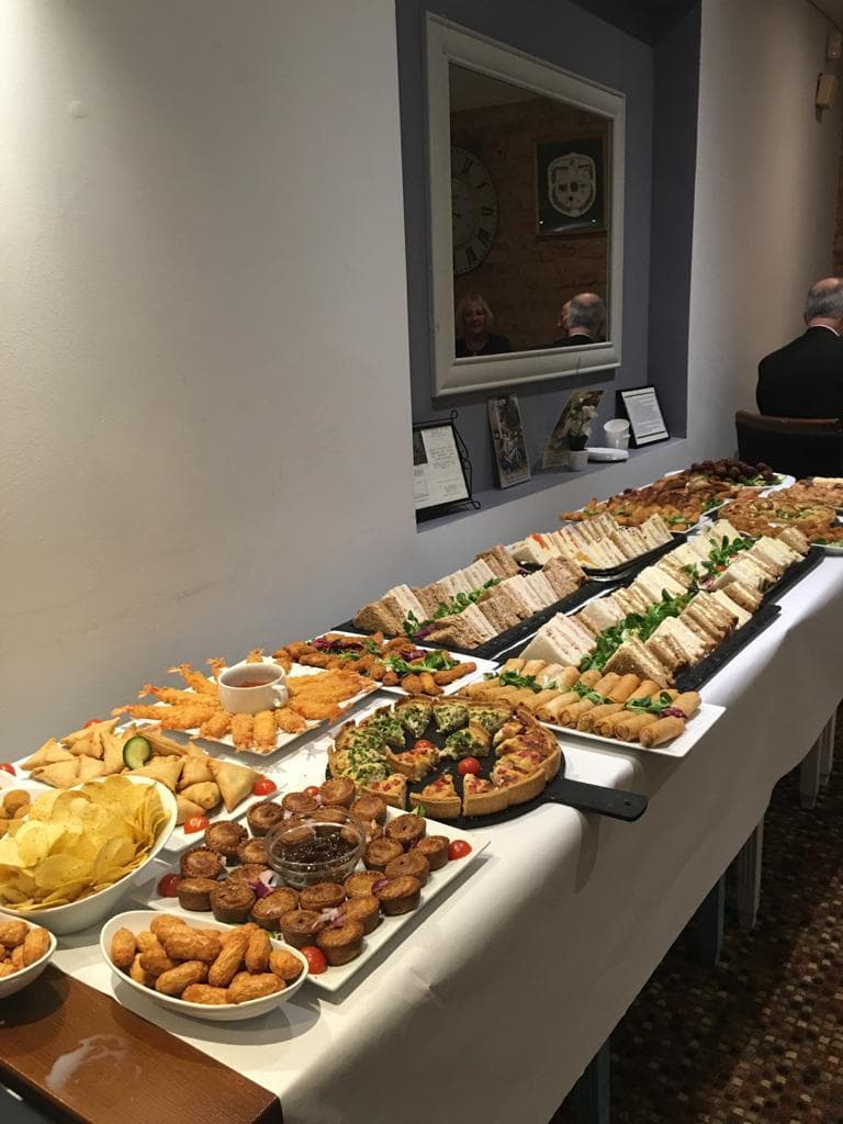 Buffet spread of sandwiches, quiche, spring rolls, samosas and crisps on a long table.