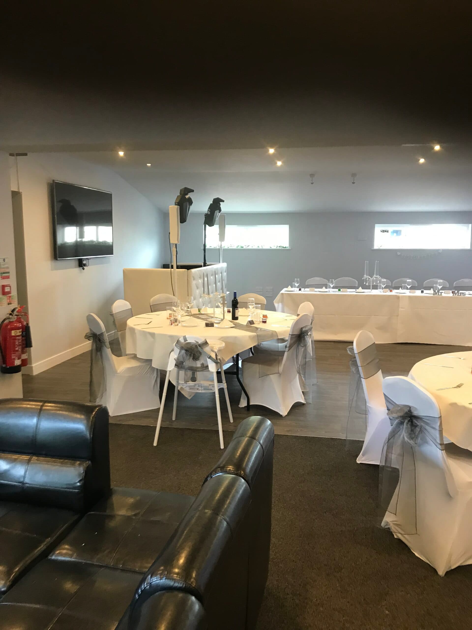 Function room set for a wedding reception with white chair covers and grey sashes.