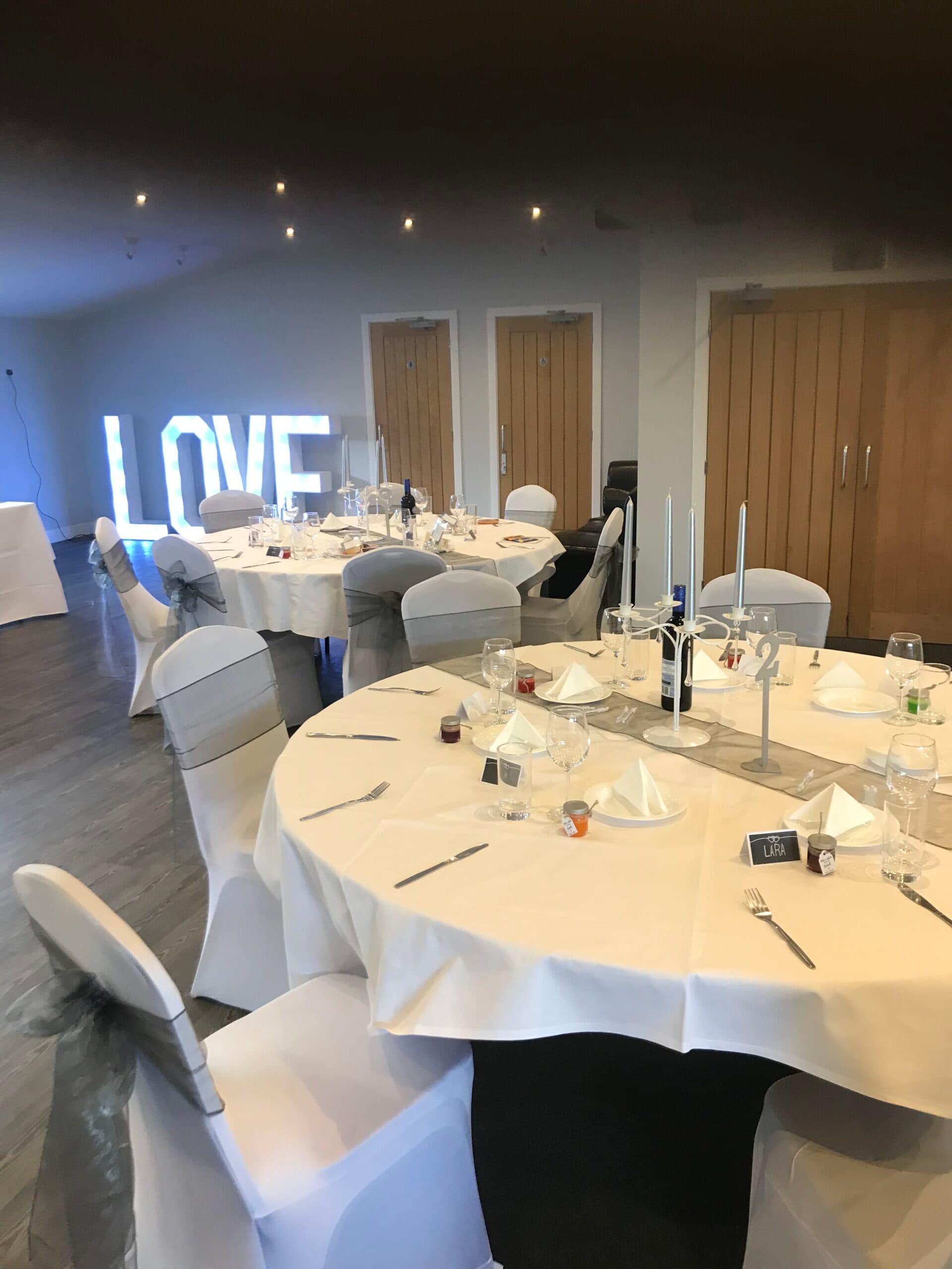Function room set for a wedding reception with illuminated LOVE letters and round tables.