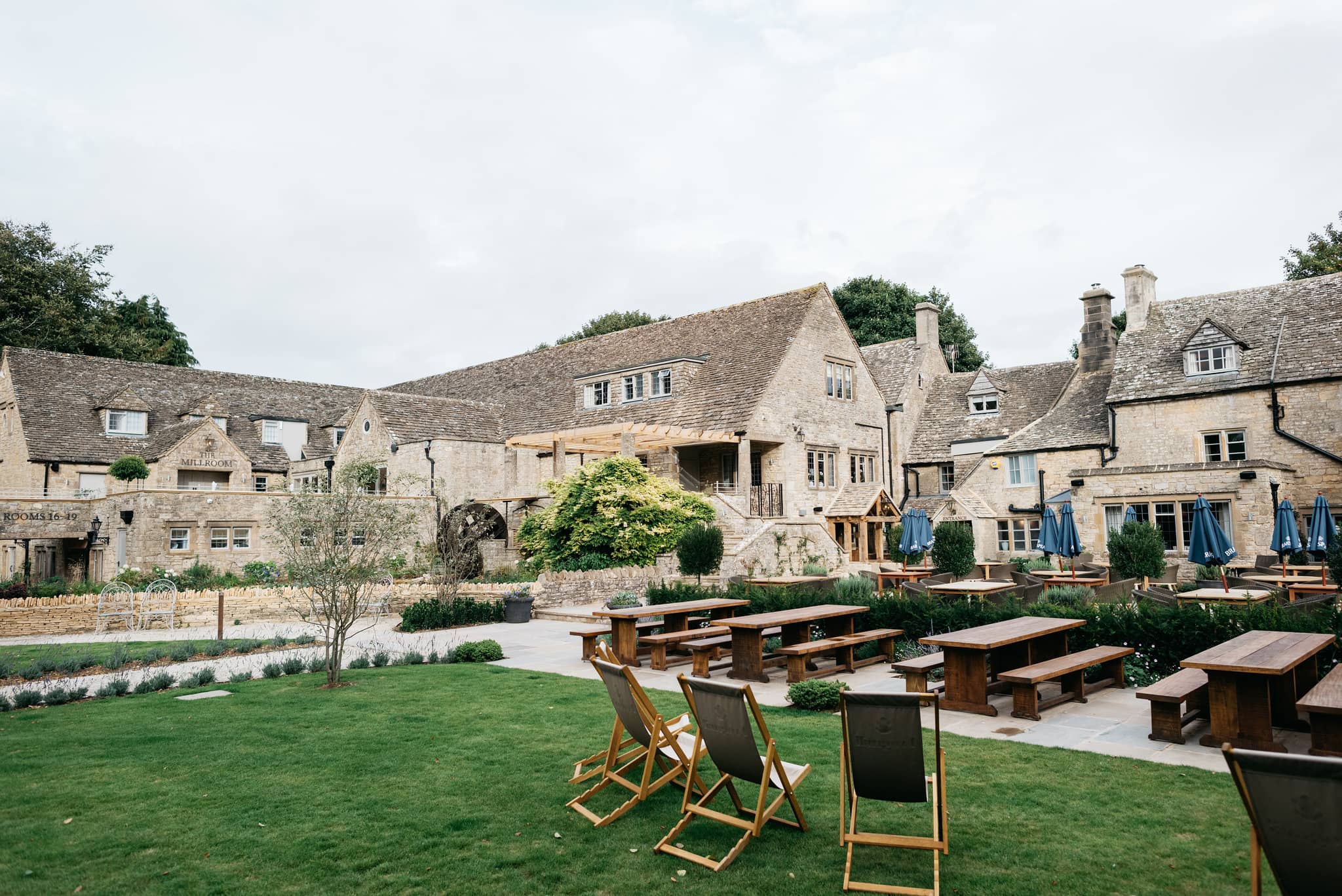 The Frogmill's lawned garden with deckchairs, picnic benches and Cotswold stone buildings.