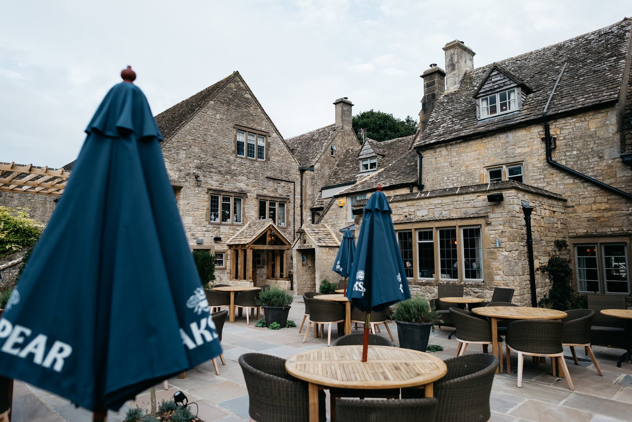 The Frogmill's stone courtyard terrace with round wooden tables and blue parasols.