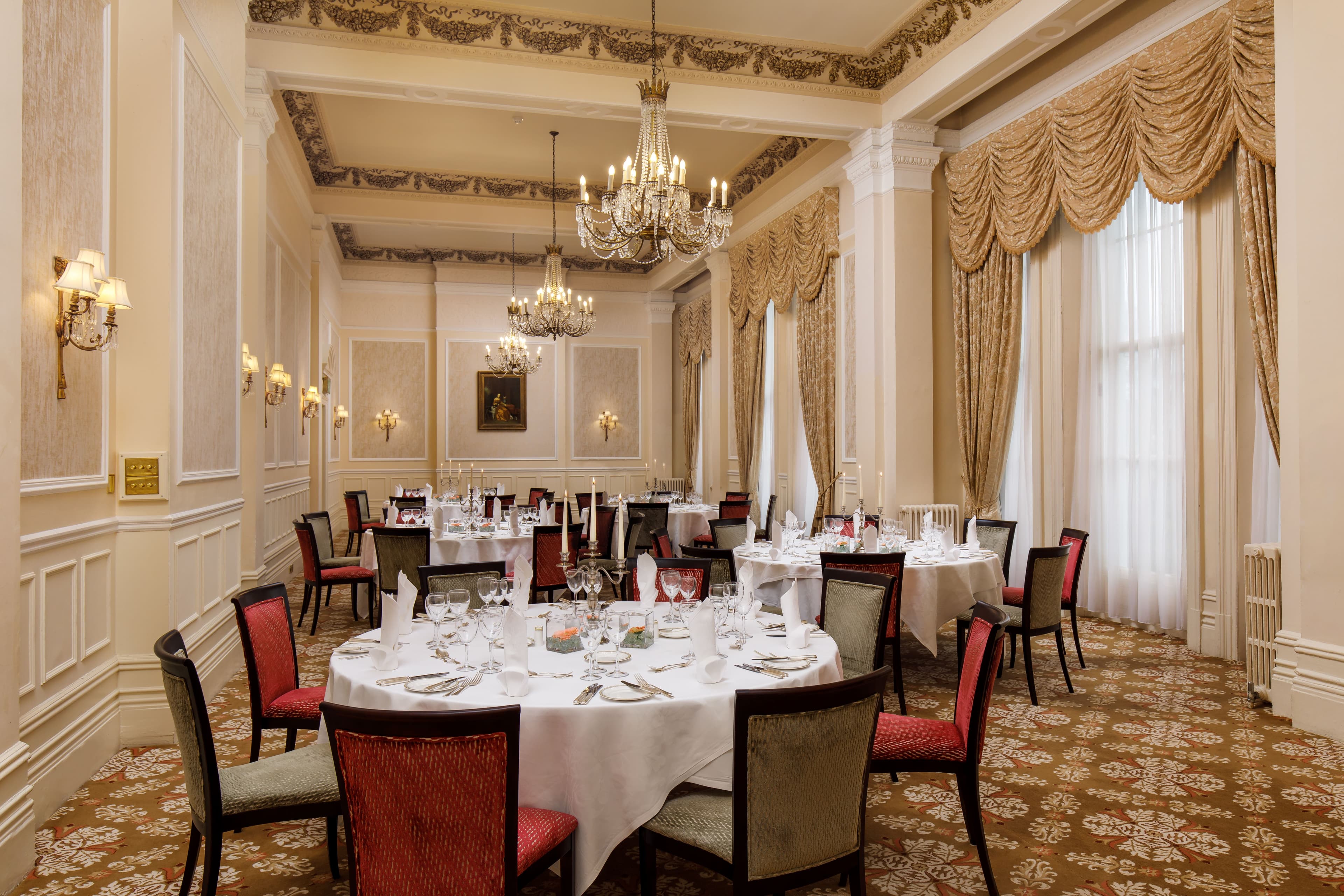 Formal private dining room with round tables, chandeliers and gold draped curtains.