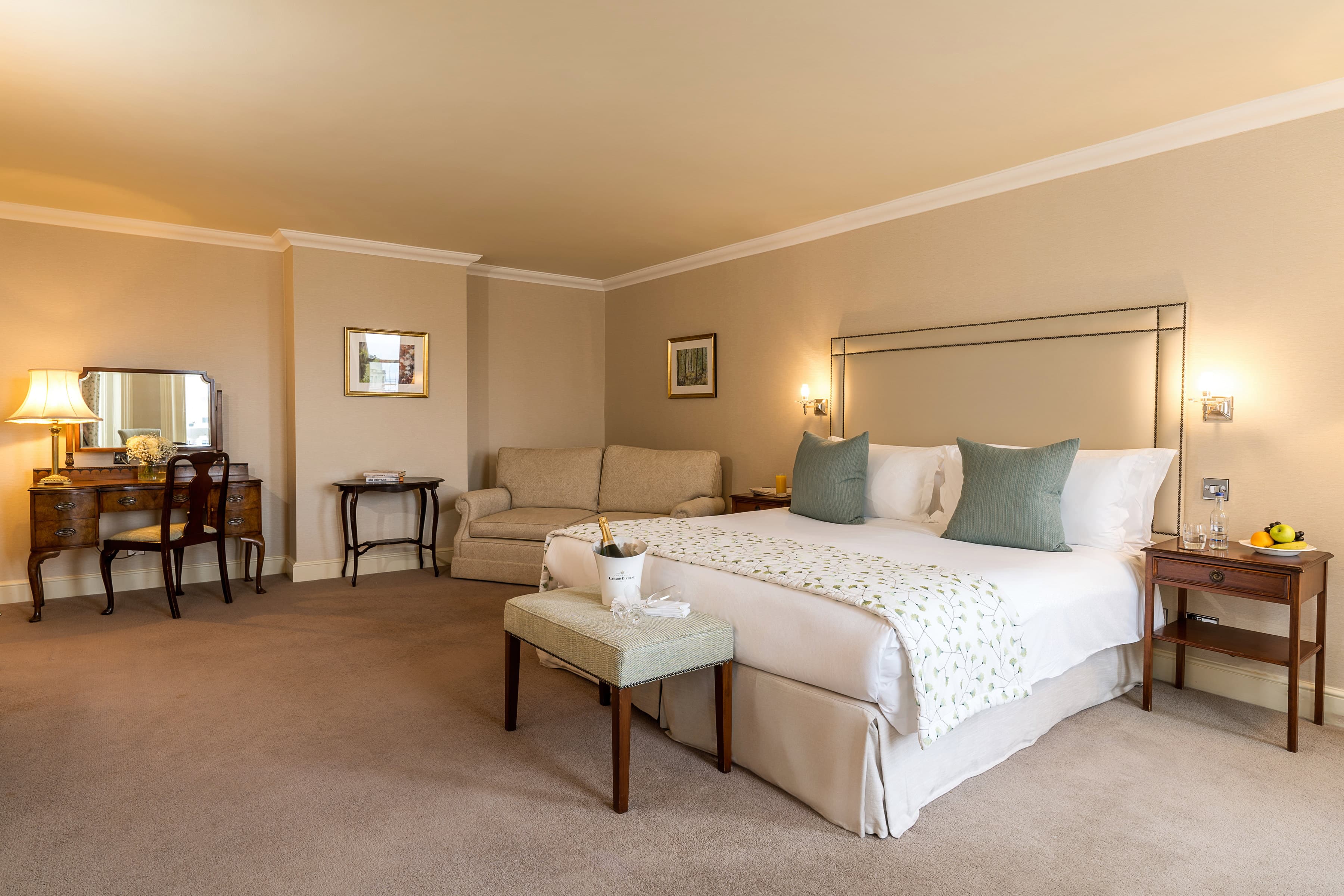 Spacious hotel double room with champagne on ice and teal cushions.