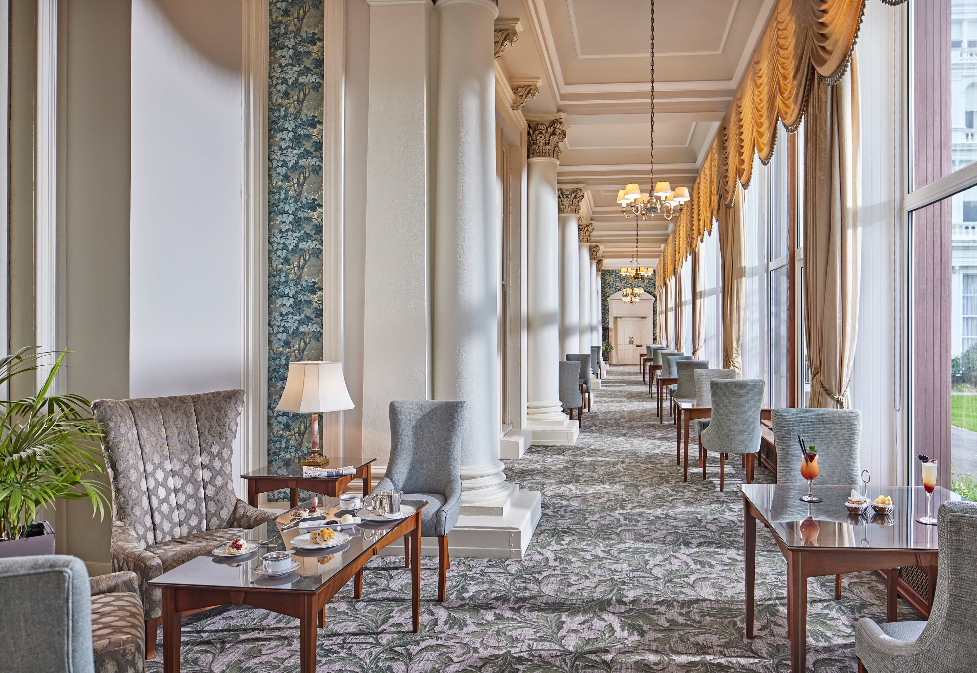 Elegant colonnaded lounge with afternoon tea set on low tables and patterned carpet.