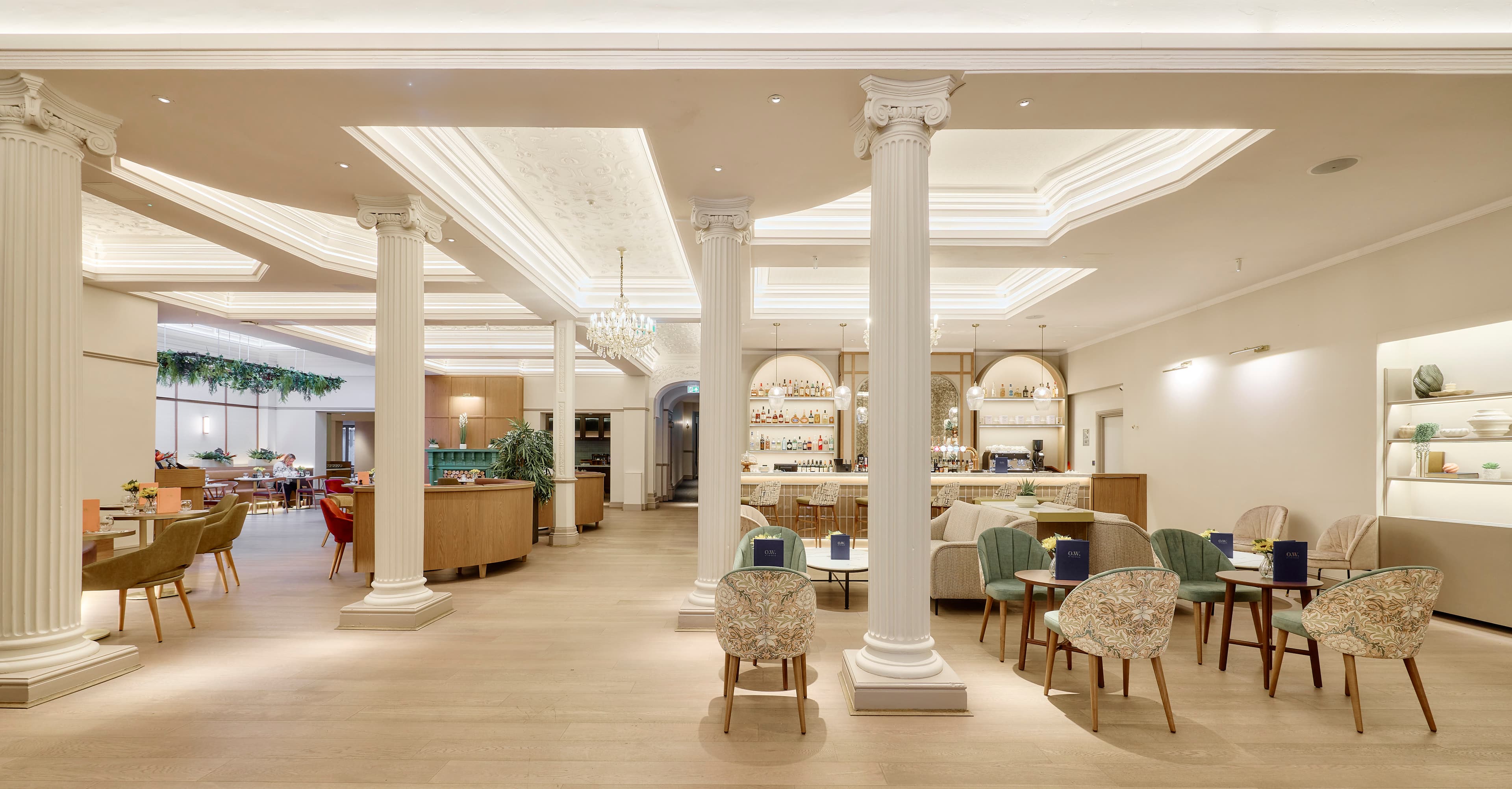 Elegant hotel lounge with white Corinthian columns, patterned armchairs and a bar beyond.