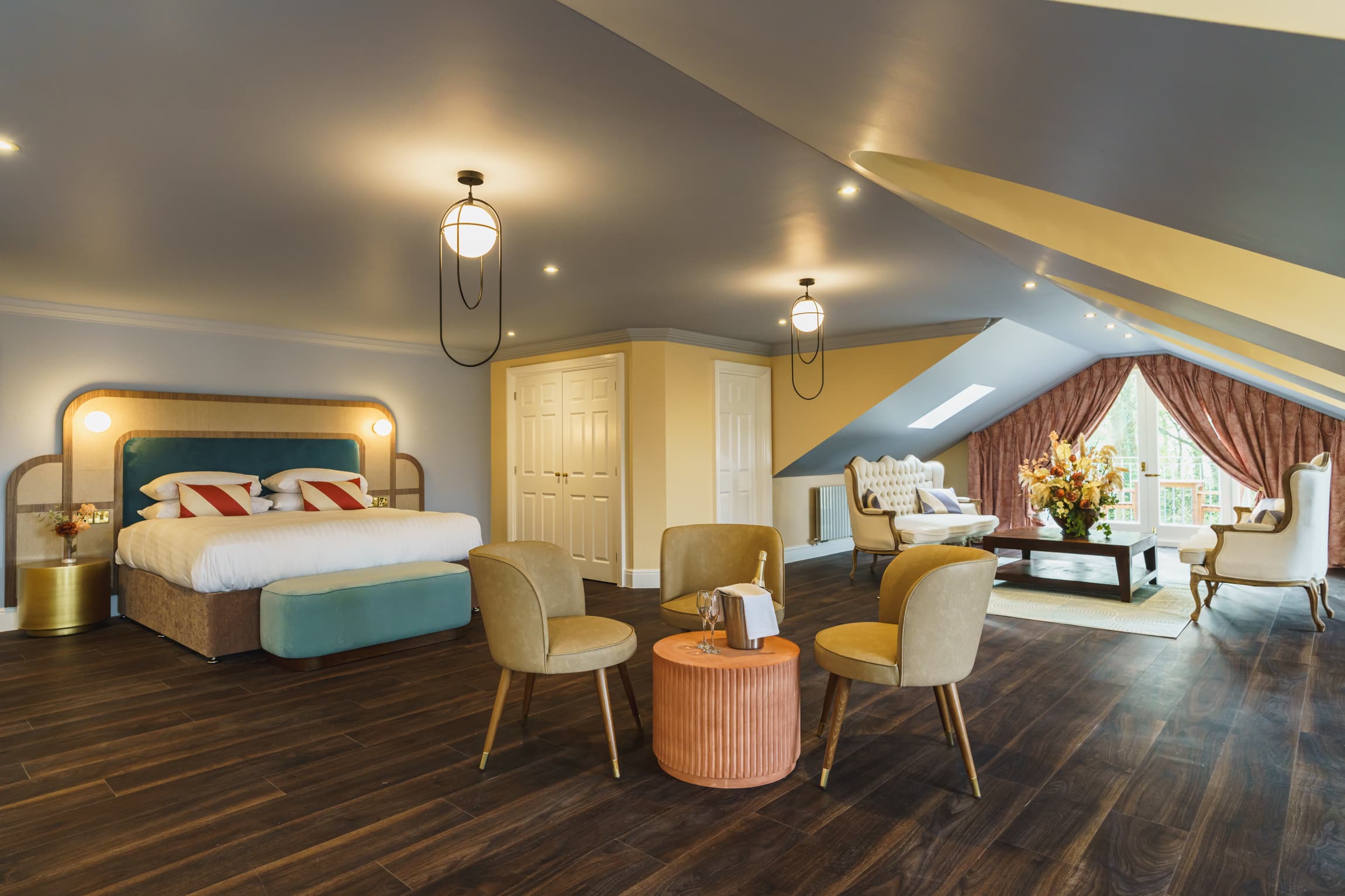 Spacious hotel suite with double bed, mustard chairs, champagne and sitting area.