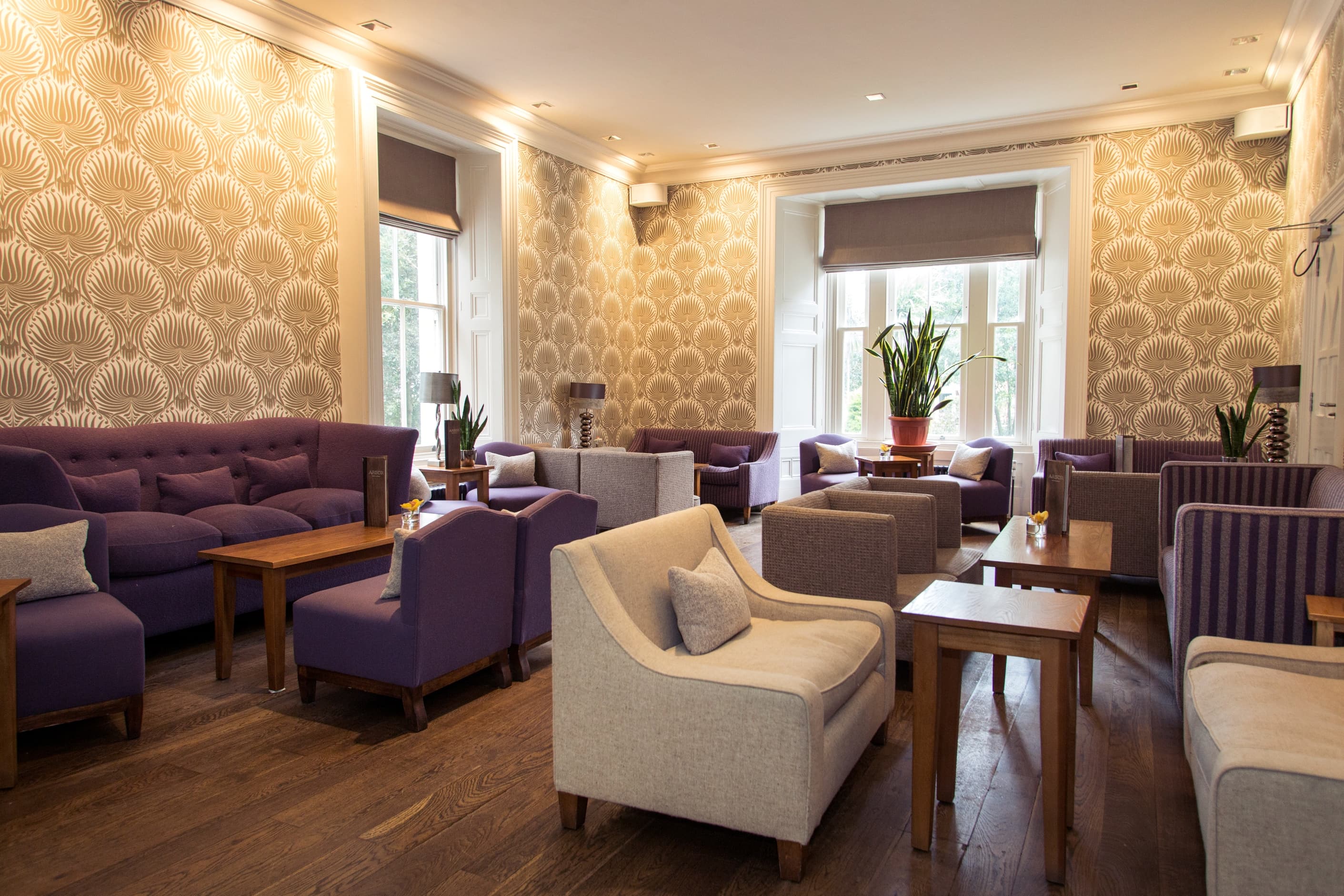 Lounge area with purple and grey armchairs, wooden floors and patterned gold wallpaper.