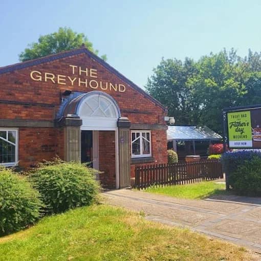 The exterior of The Greyhound pub in red brick with a wooden fence and garden.