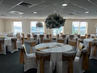 Function room set for a celebration with round tables and gold chair sashes.