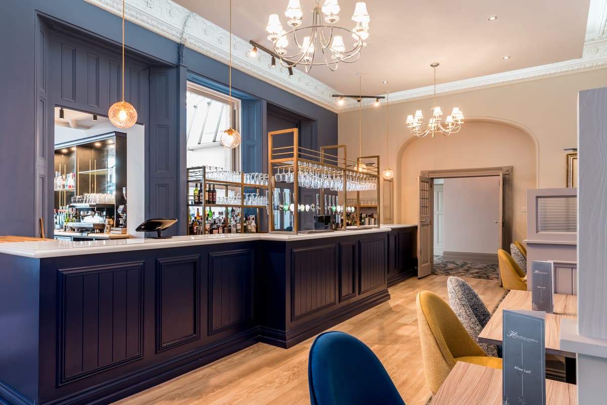 The Headland Hotel bar with dark panelling, brass glass racks and chandelier lighting.