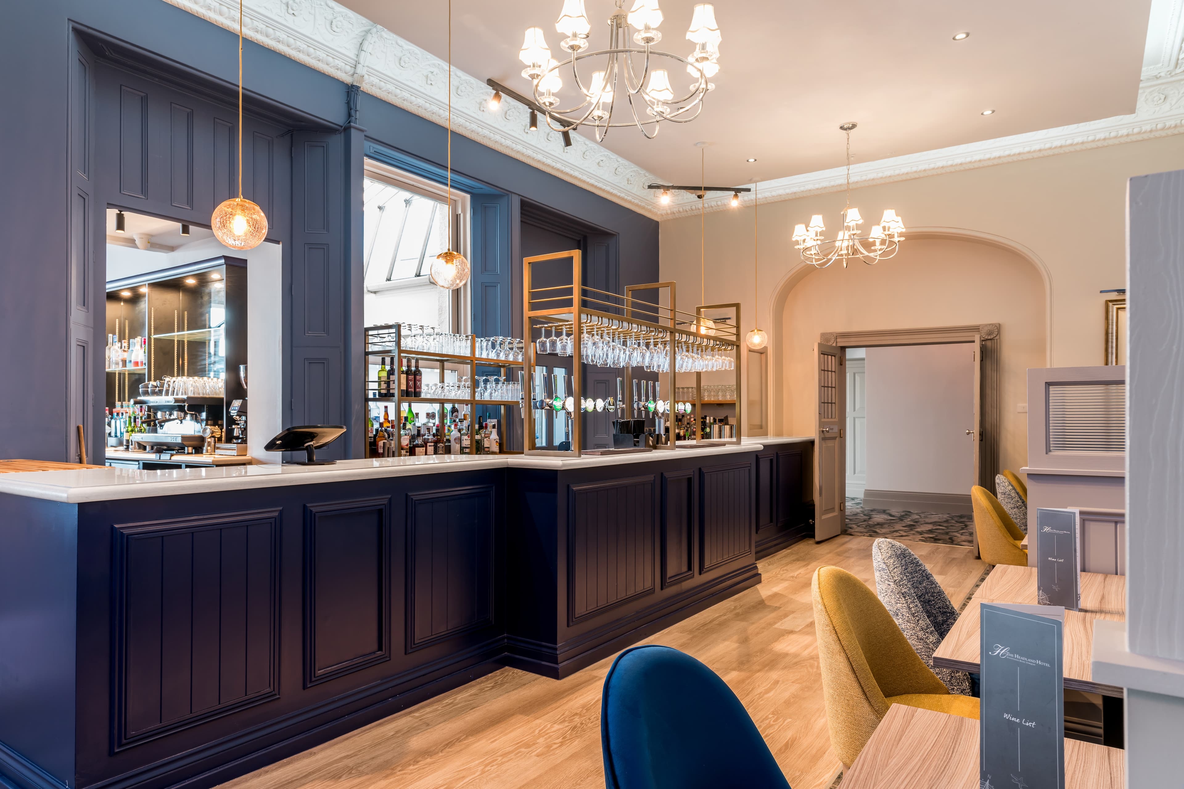The Headland Hotel bar with dark panelling, brass glass racks and chandelier lighting.