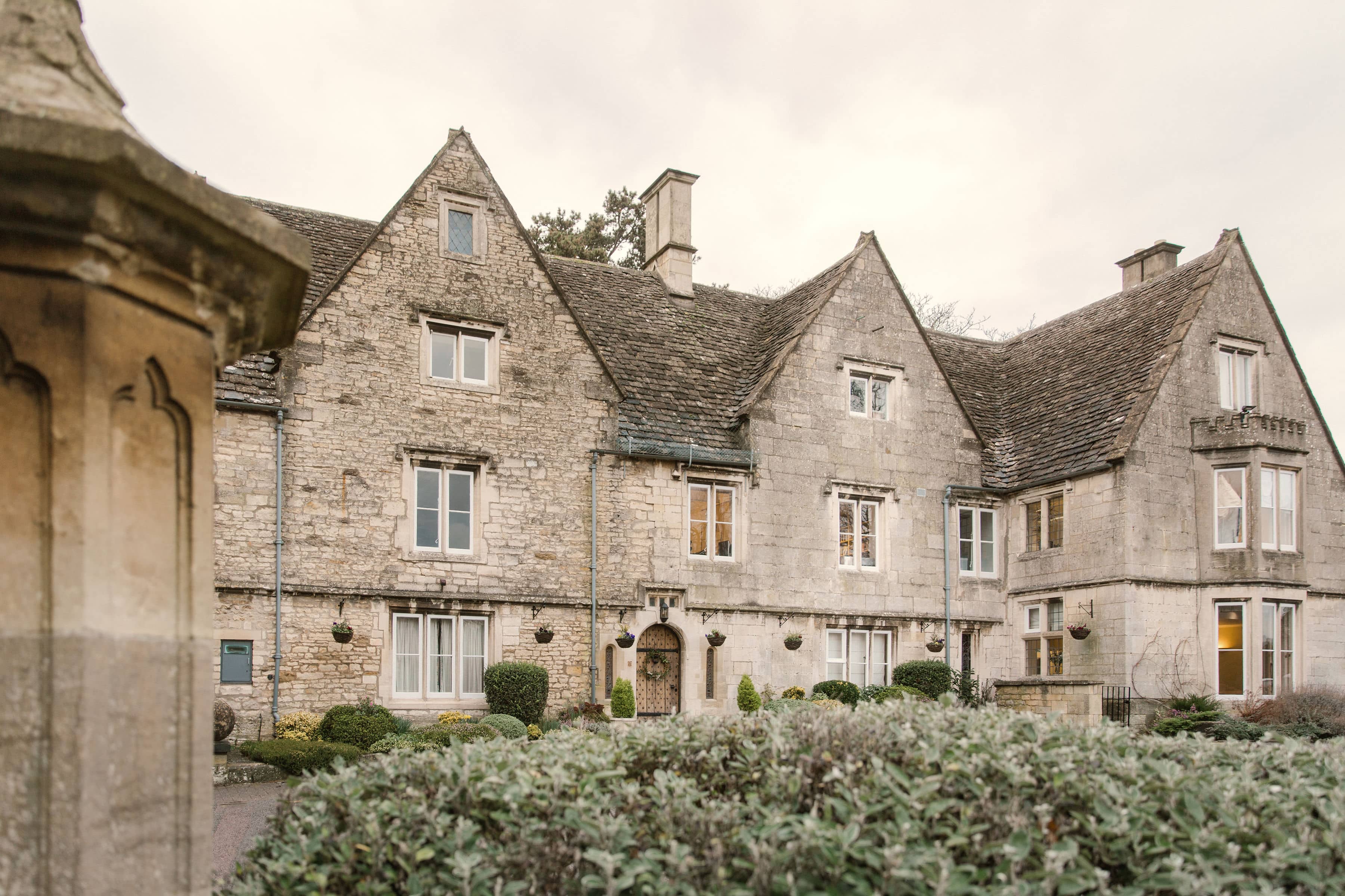 The stone exterior of The Hill manor house in Stroud with manicured hedging and shrubs.
