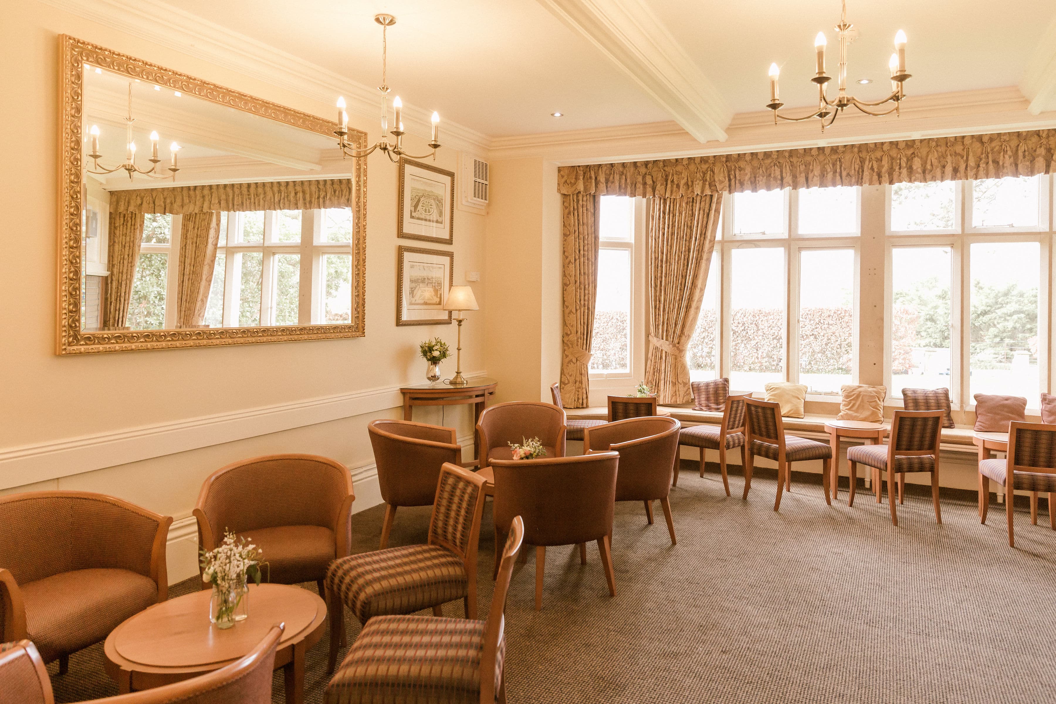 Bright bar area at The Hill with upholstered armchairs, chandeliers and large sash windows.