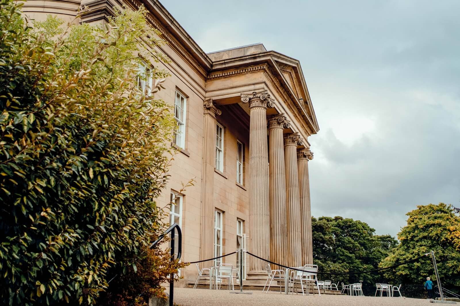 The Mansion's sandstone neoclassical exterior with Ionic columns and outdoor seating area.