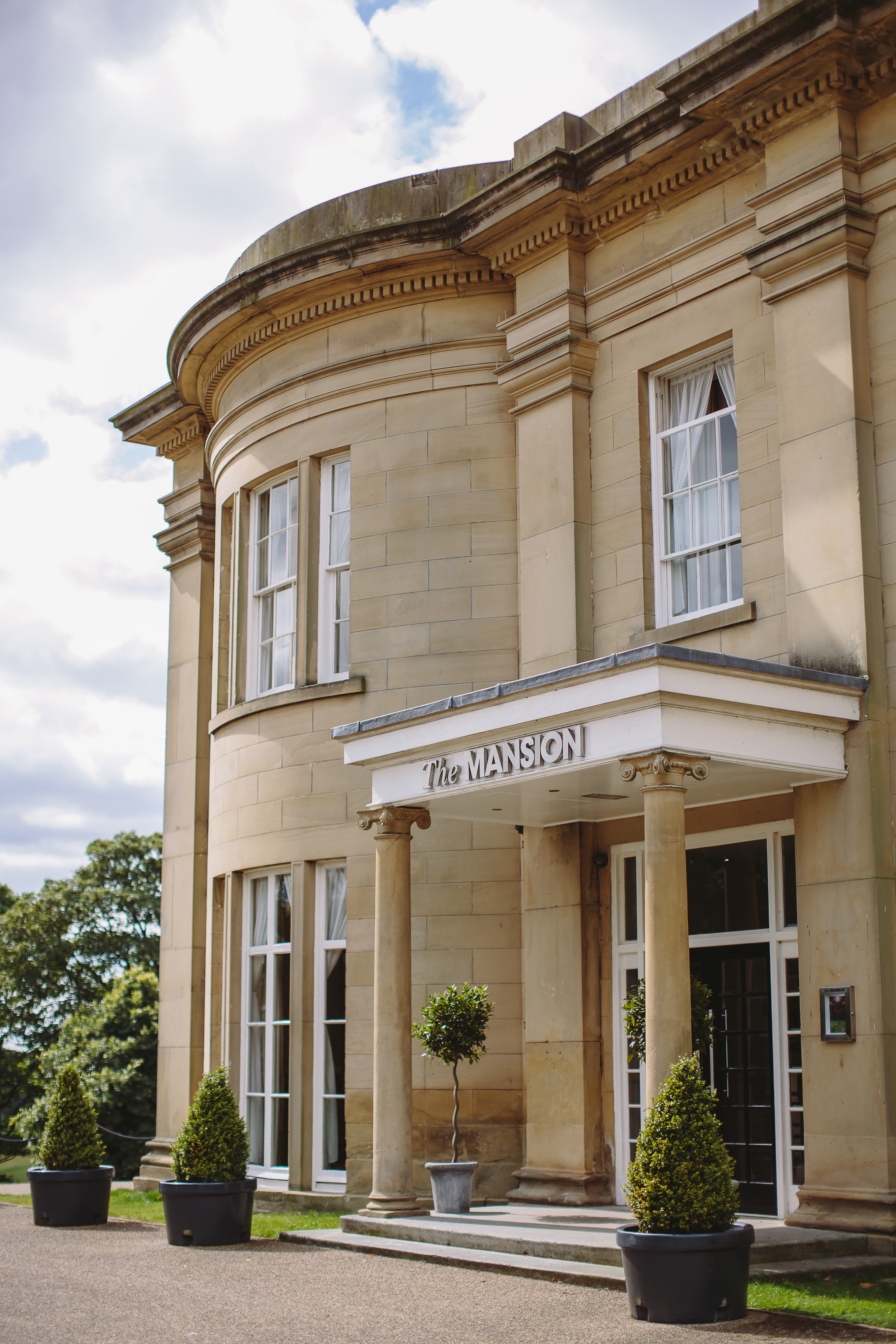 The sandstone exterior of The Mansion Leeds with Corinthian columns and topiary plants.