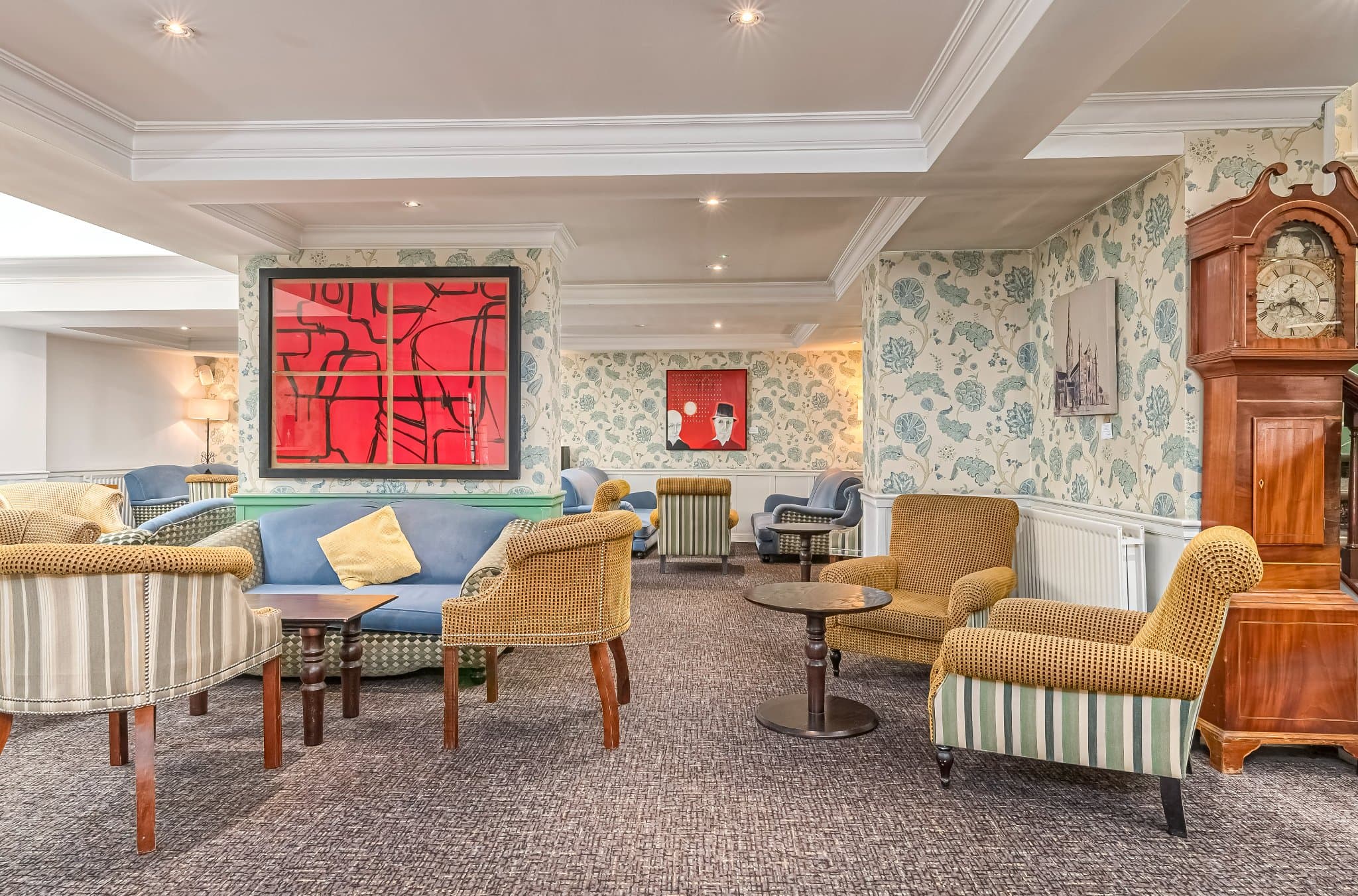 Hotel lounge with patterned wallpaper, mustard armchairs, a blue sofa and bold red artwork.