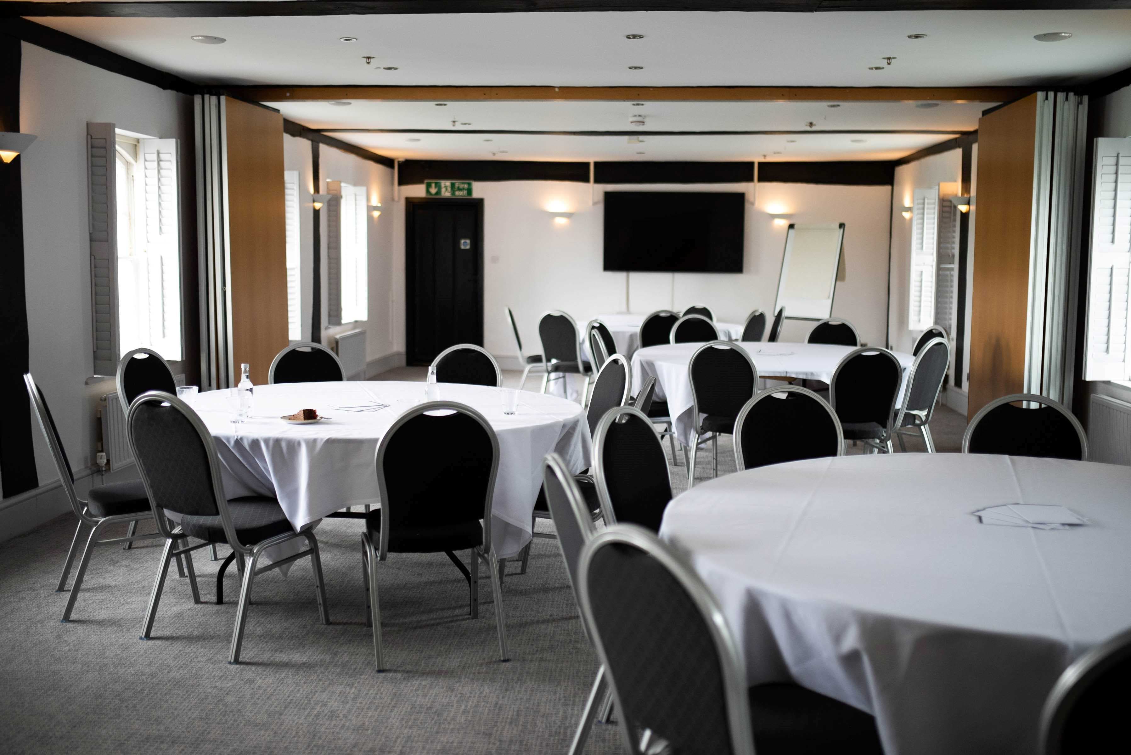 Function room at The Mill Hotel with round tables, banquet chairs and a wall-mounted screen.