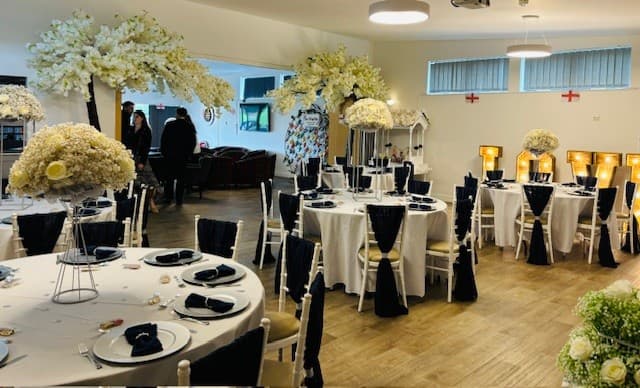 Function room laid for an event with round tables, black chair sashes and tall floral centrepieces.