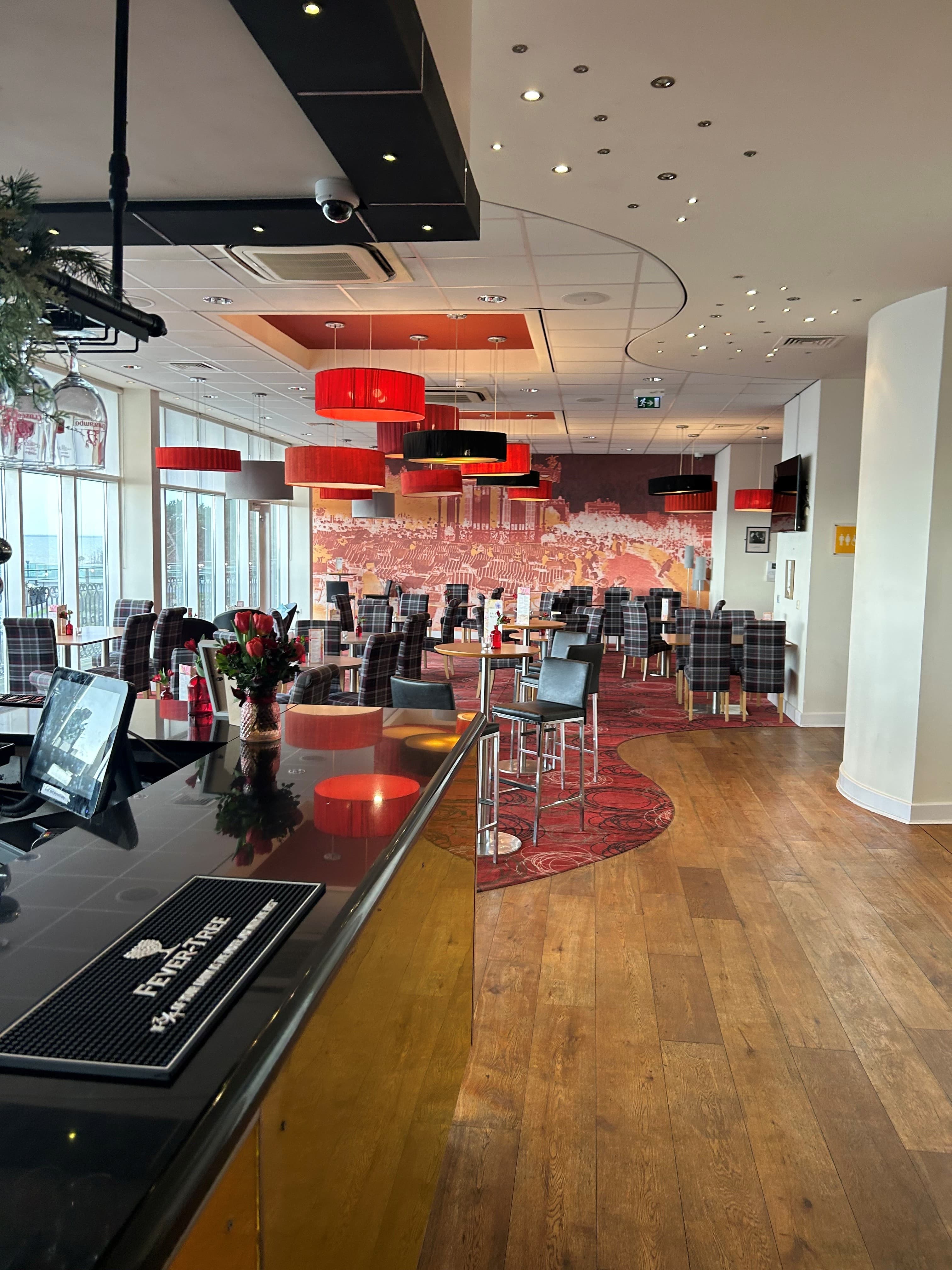Spacious bar and dining area with red pendant lights and tartan upholstered chairs.