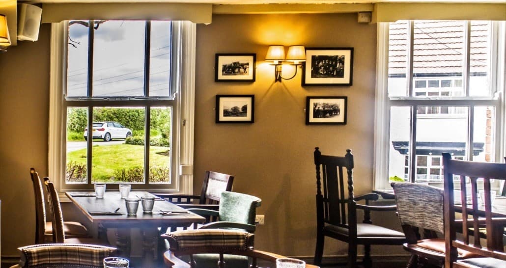 Dining area at The Plough with wooden chairs, set tables and black and white prints.