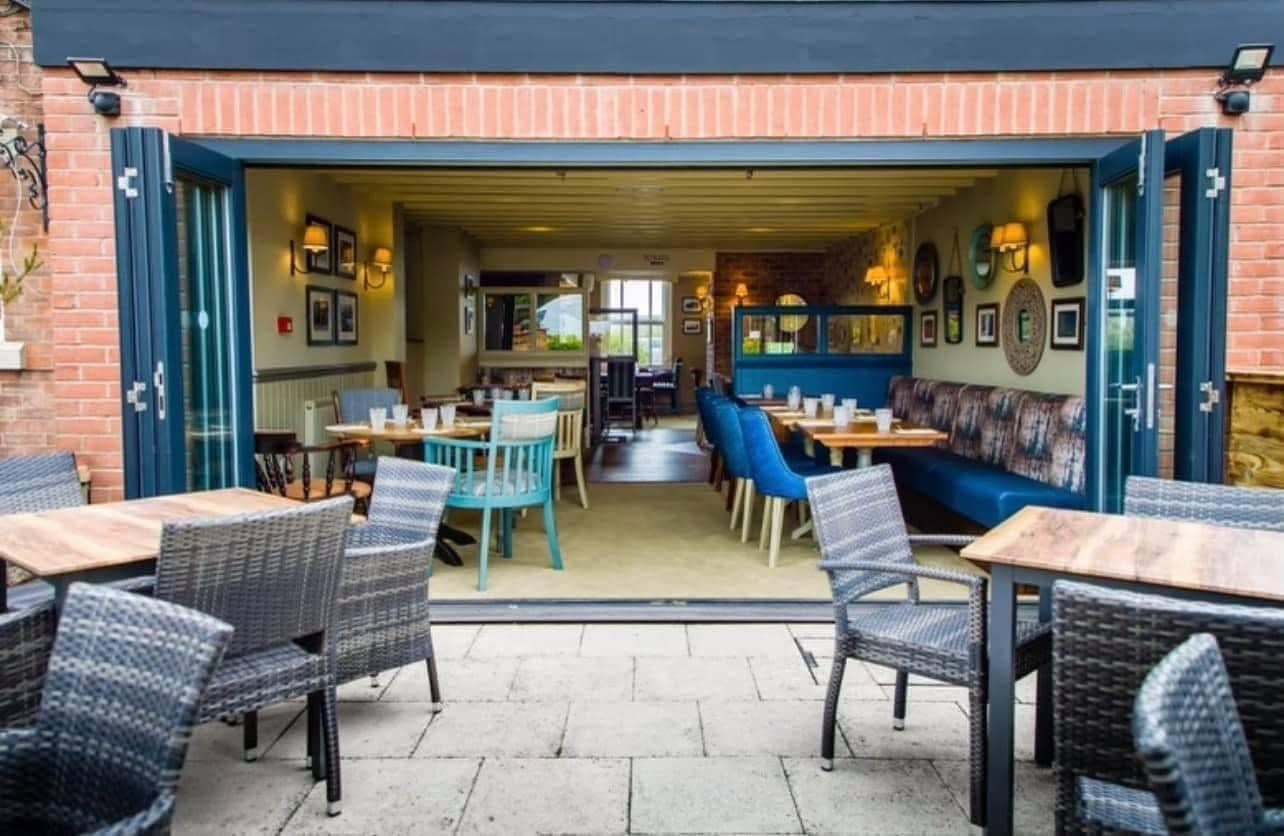 Paved terrace with rattan chairs leading into the dining room through open bifold doors.