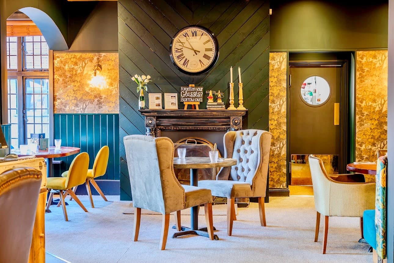 Lounge area at The Radcliffe with mismatched armchairs, a fireplace and large wall clock.