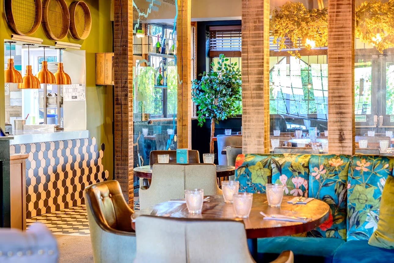 Bright restaurant interior with floral banquette seating, round wooden tables and copper pendant lights.