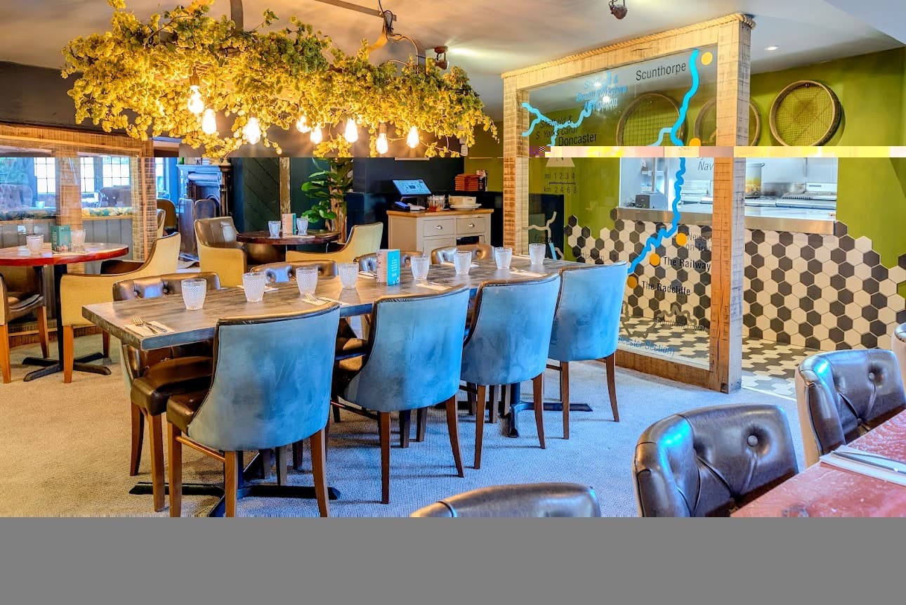 Dining room with a long table, blue chairs and a hanging hop display overhead.