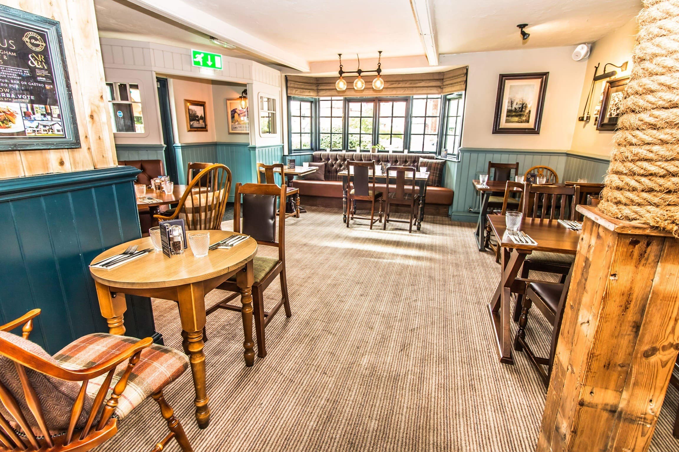 Carpeted dining area at The Railway with wooden tables, tartan chairs and bay window seating.